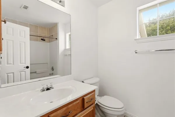 Bathroom featuring a wood-finish vanity with an integrated sink, a large mirror, and a shower-tub combination with tile surround