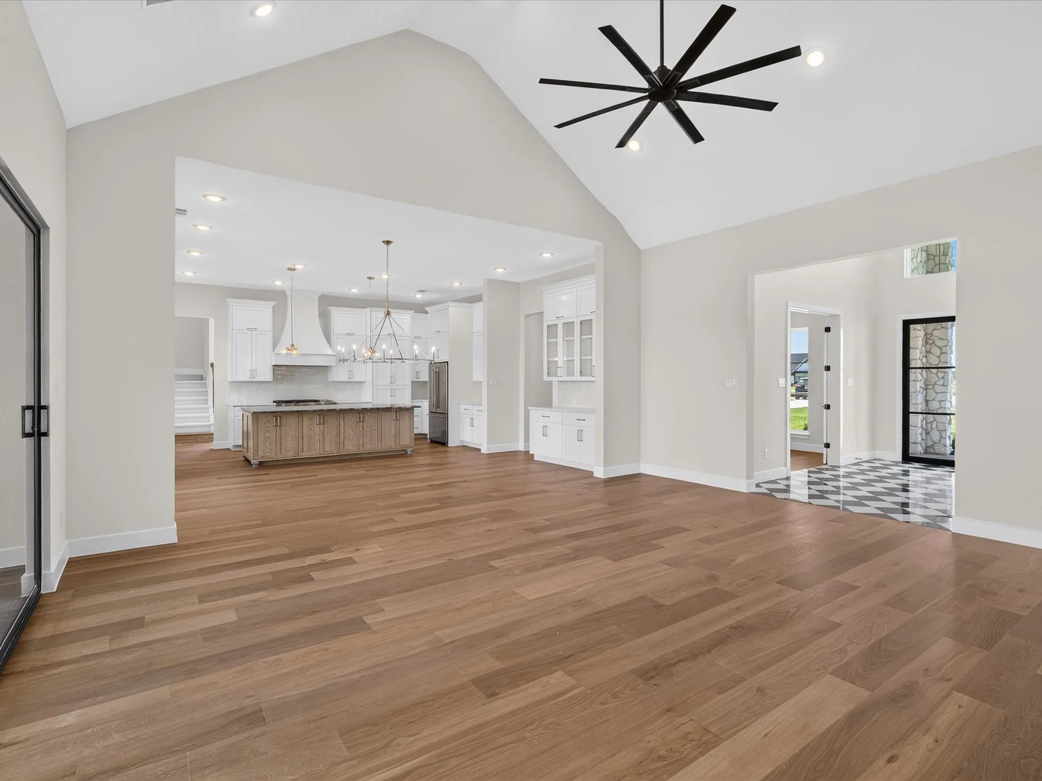Vaulted ceiling with an oversized ceiling fan, wood-finish flooring, built-in cabinetry, recessed lighting, and an open layout to the kitchen