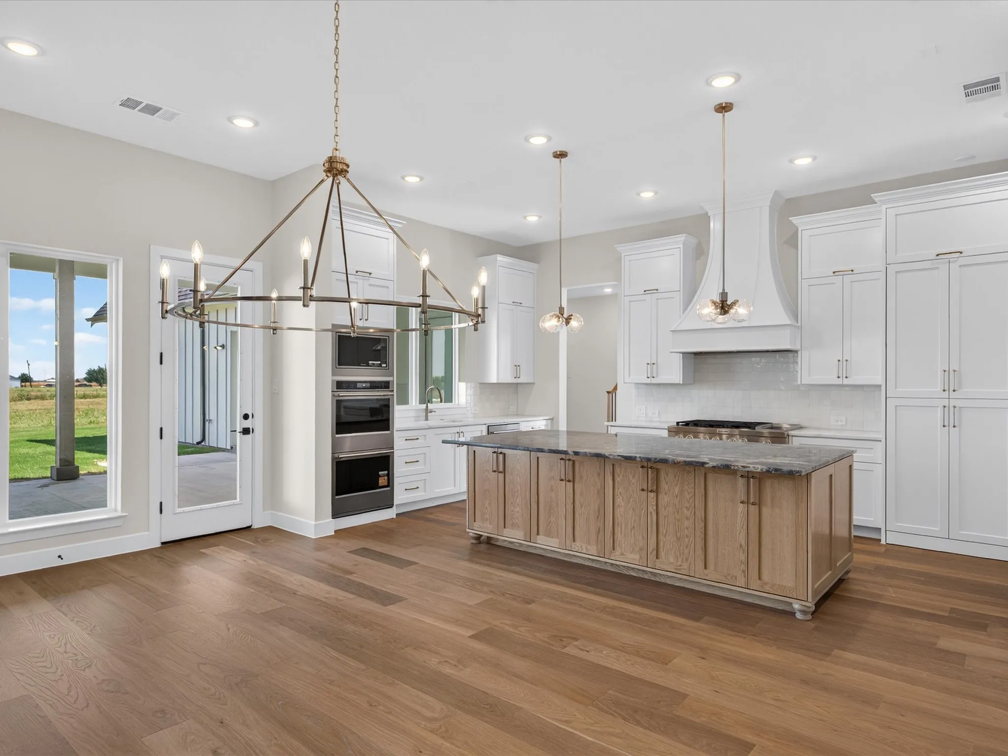Wood-finish flooring, white cabinetry, built-in stainless steel appliances, stone countertops, and a central island with paneling