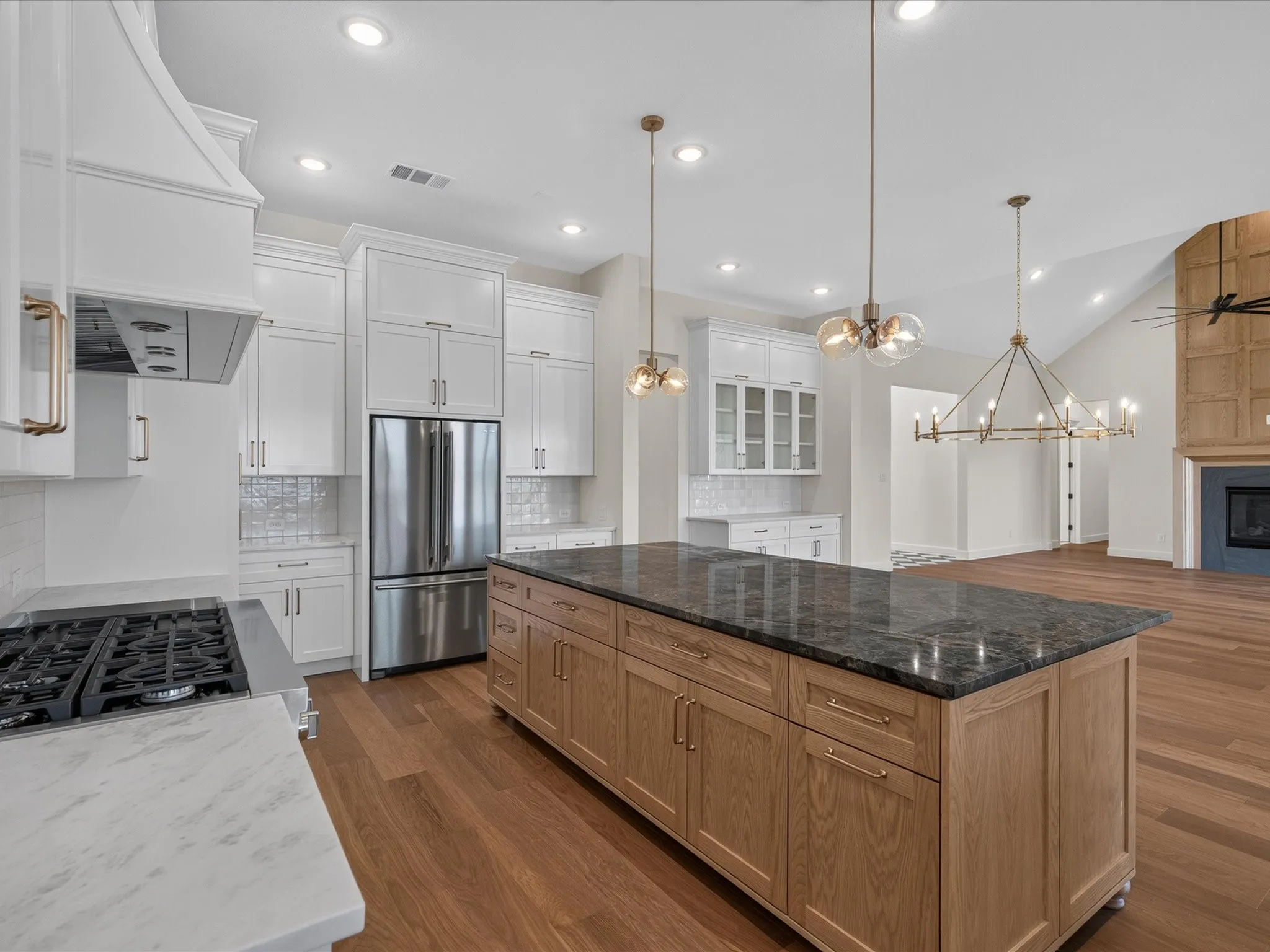 Gourmet kitchen featuring a wood-finish island with a dark stone countertop, white shaker cabinetry, stainless steel appliances, and wood-finish flooring