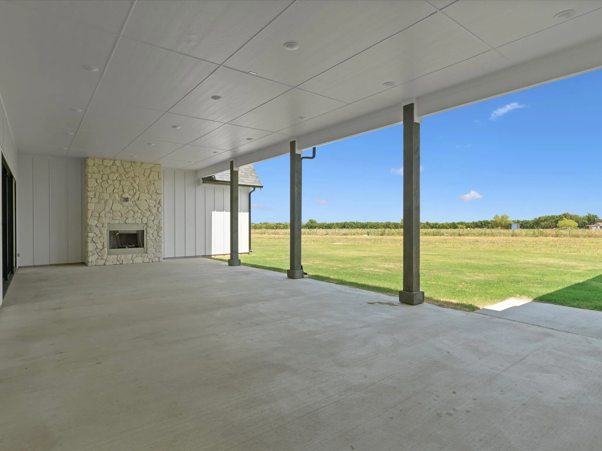 Expansive concrete patio with a stone-clad fireplace and recessed lighting