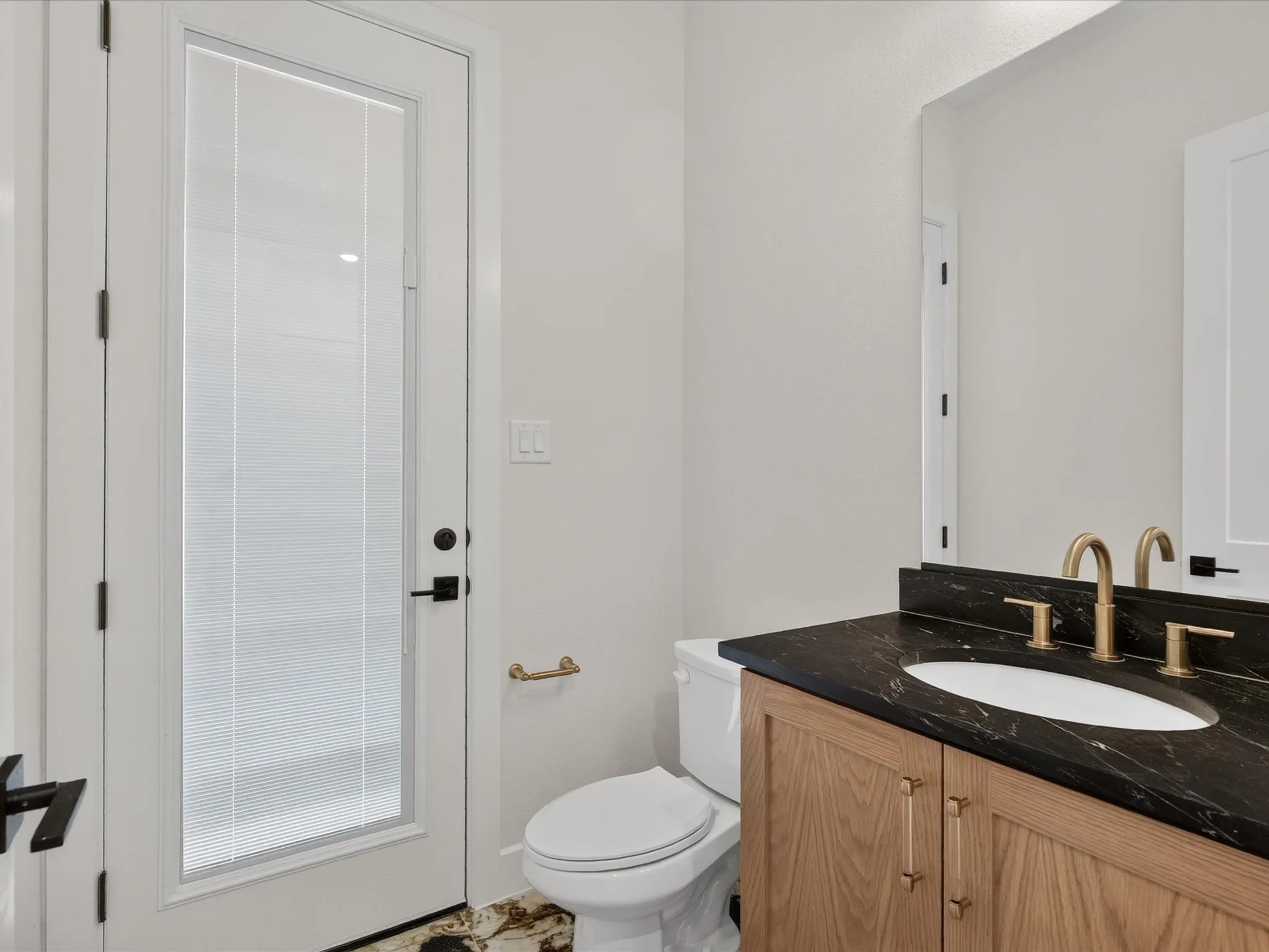 Wood-finish vanity with a black stone countertop, gold-tone faucet, integrated oval sink, and a full-height mirror