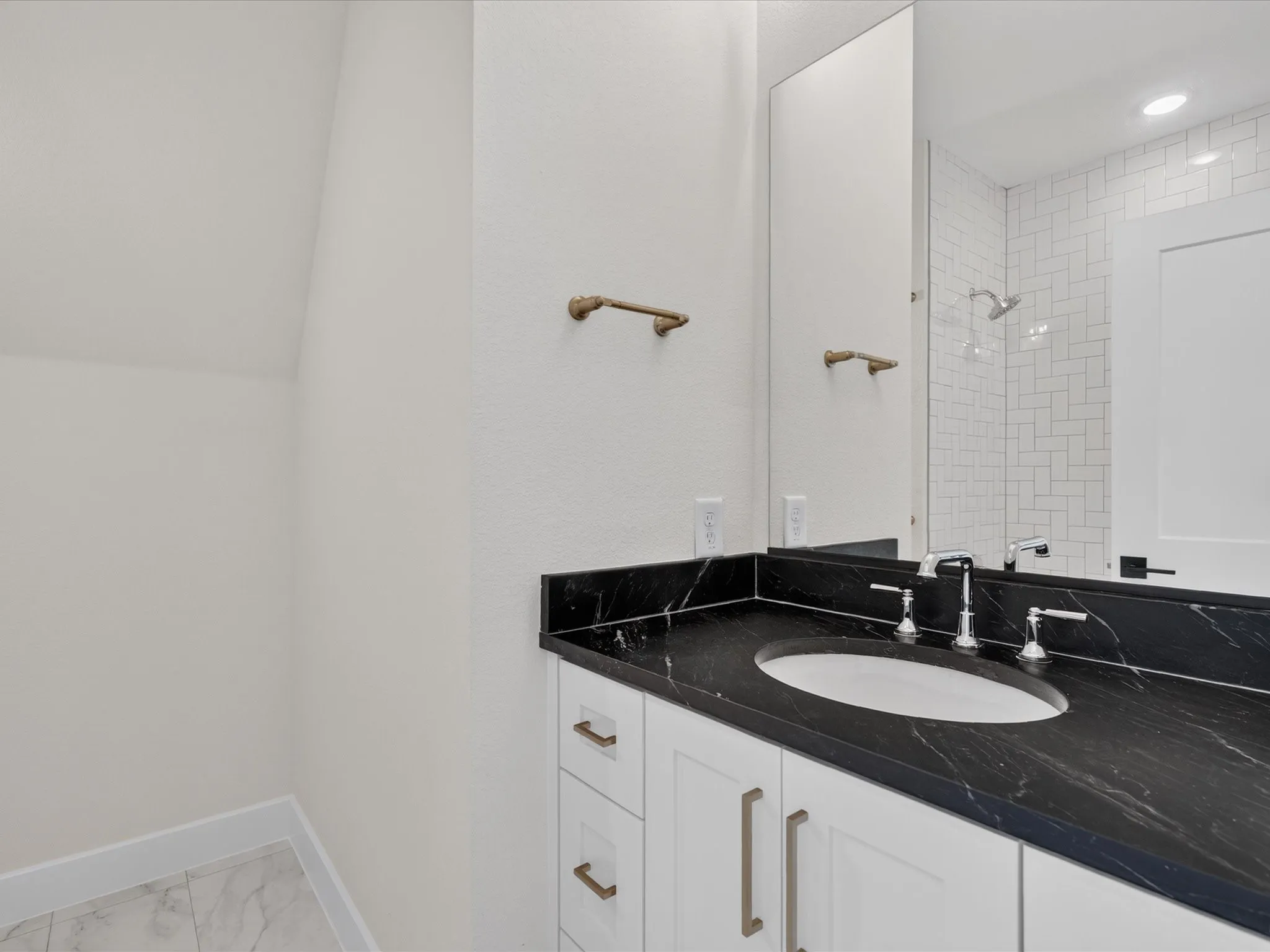 Modern bathroom featuring a white vanity with dual drawers, black stone countertop with integrated oval sink, and chrome hardware
