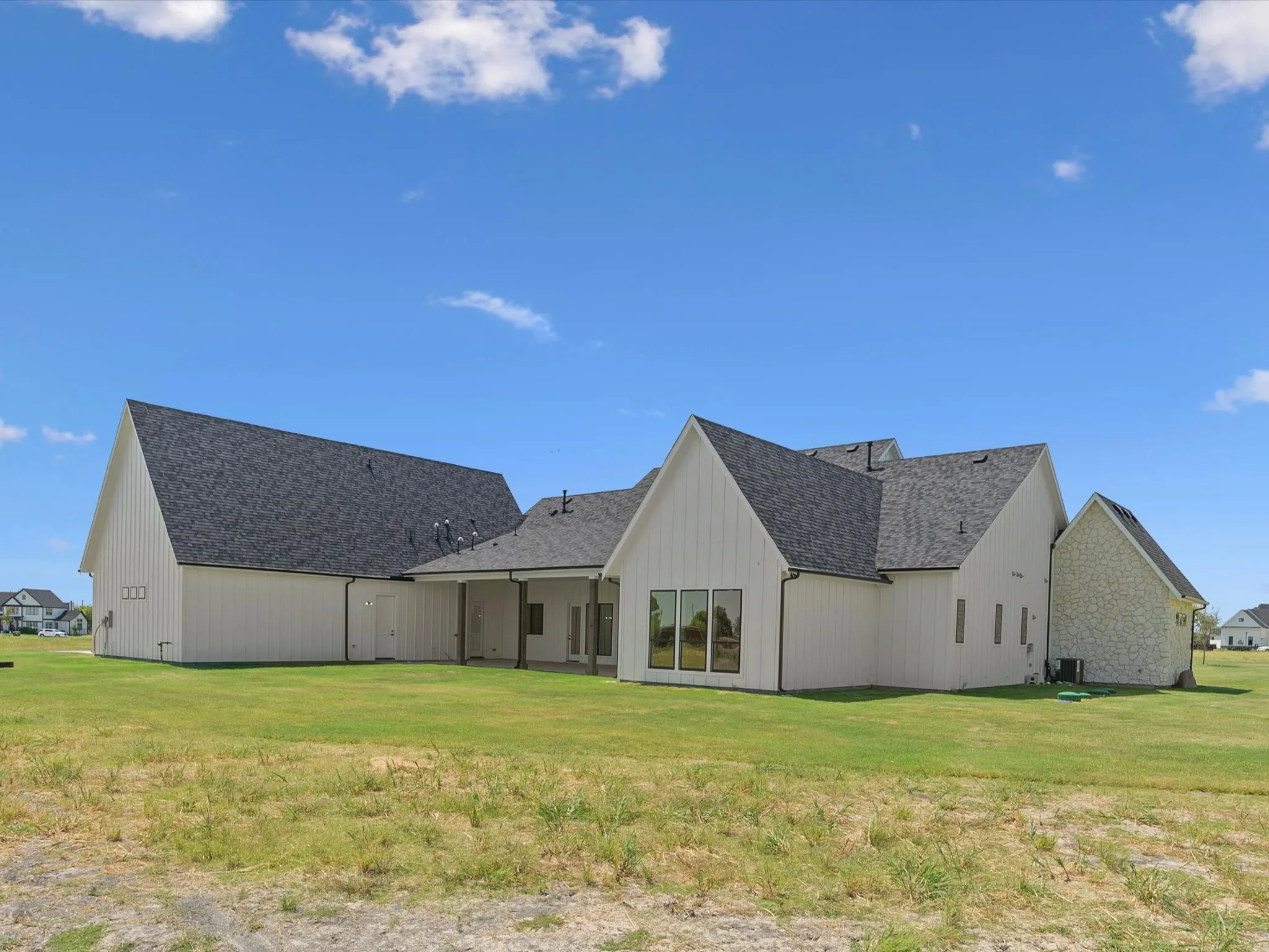 Expansive rear exterior featuring white board and batten siding, stone accents, multiple large windows, and a covered patio