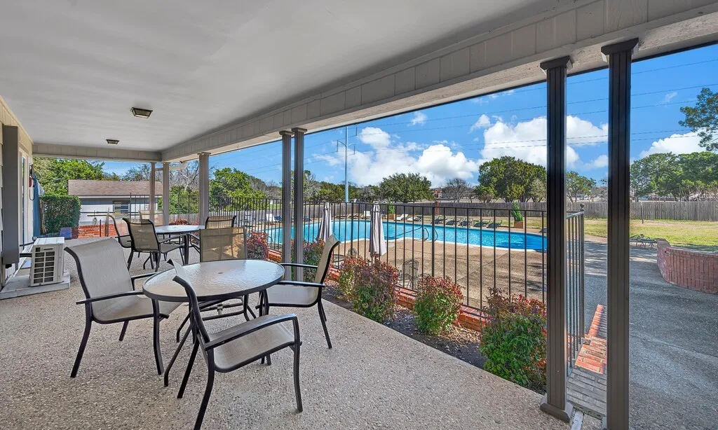 Spacious covered patio with exposed aggregate concrete flooring, featuring a black metal fence and landscaping at Pool & Clubhouse