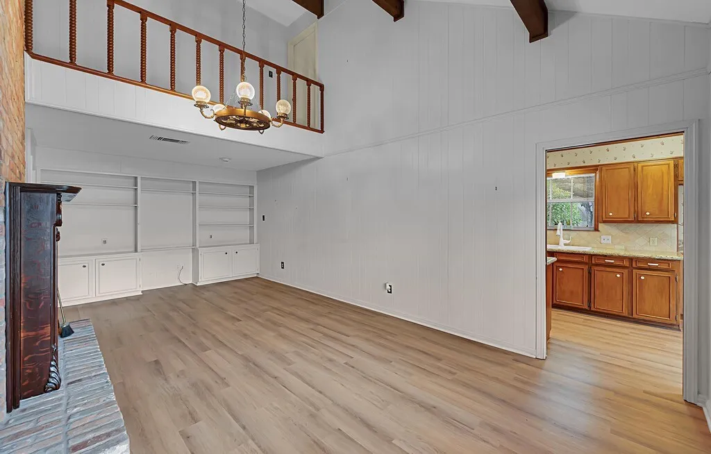 Living area featuring vaulted ceilings with exposed wood beams, luxury vinyl plank & a brick fireplace with a carved wood mantel