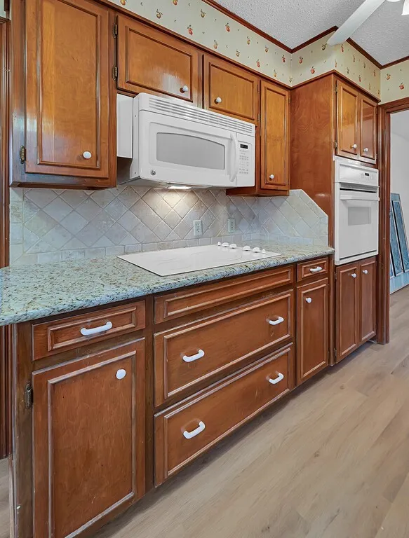 Kitchen featuring wood cabinetry, light-toned countertops, a tile backsplash, and light wood-finish flooring