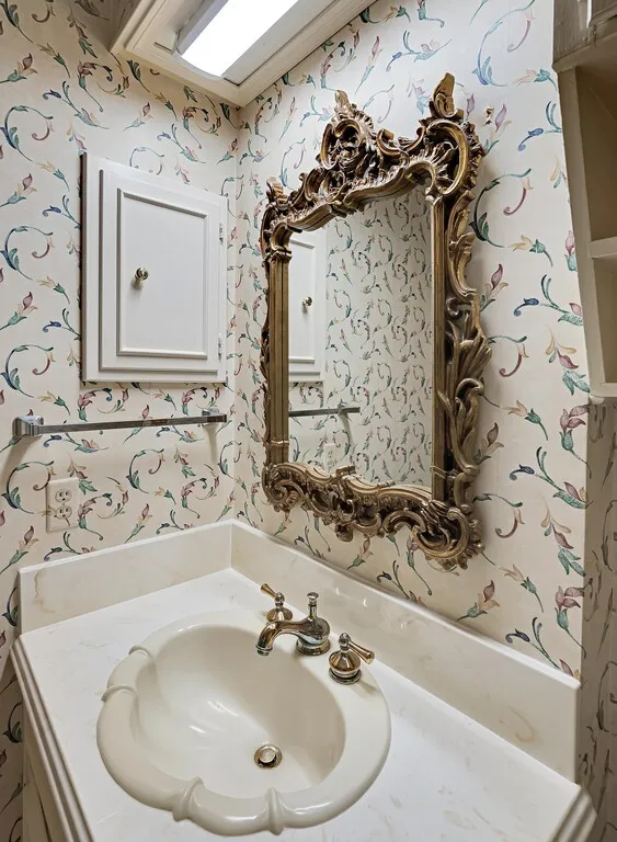Ornate gold-framed mirror over a vanity with a white-finish countertop and an oval drop-in sink