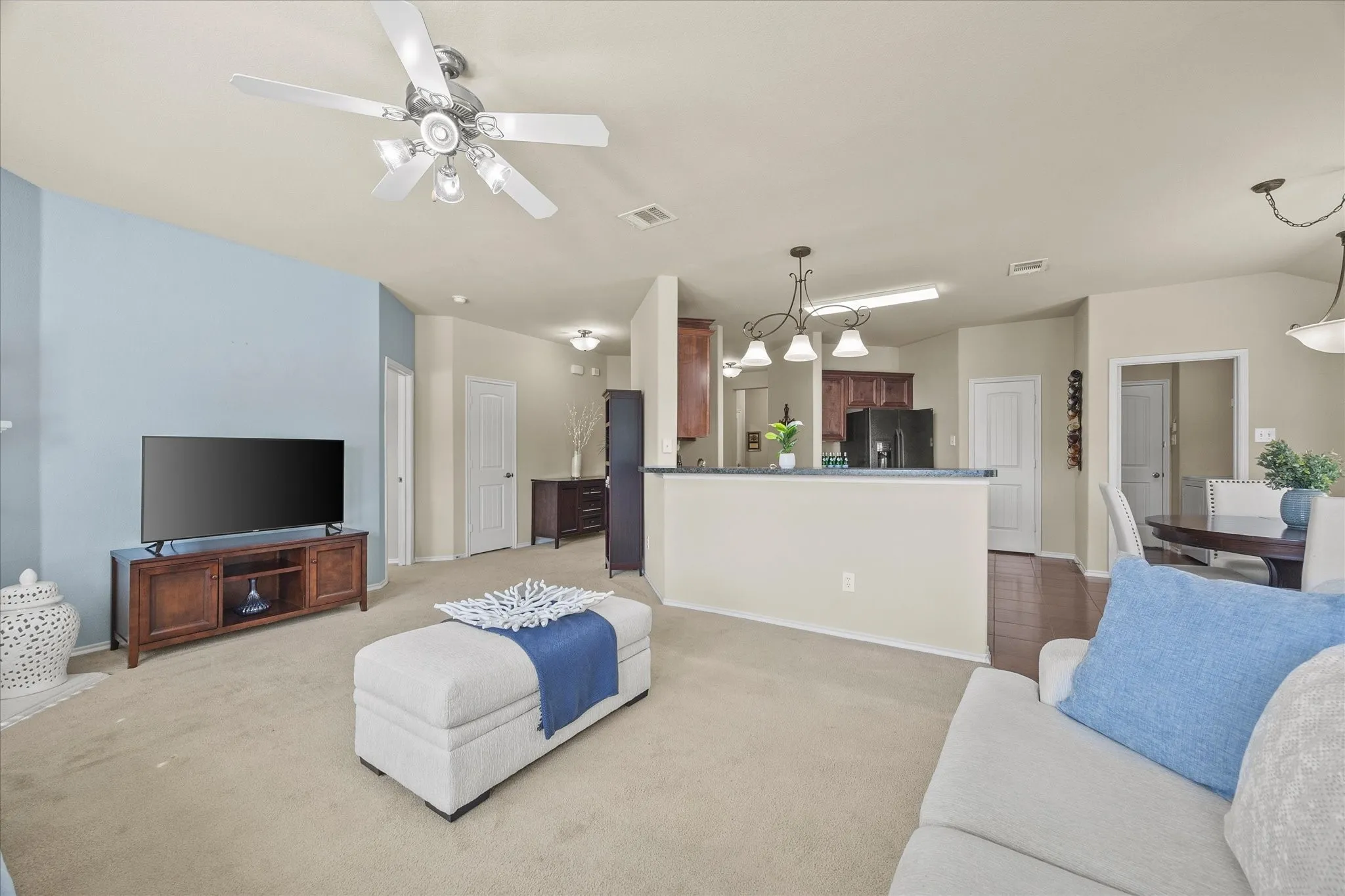 Open-concept living area with a ceiling fan light fixture, light-toned carpet flooring, and a half wall separating the spaces