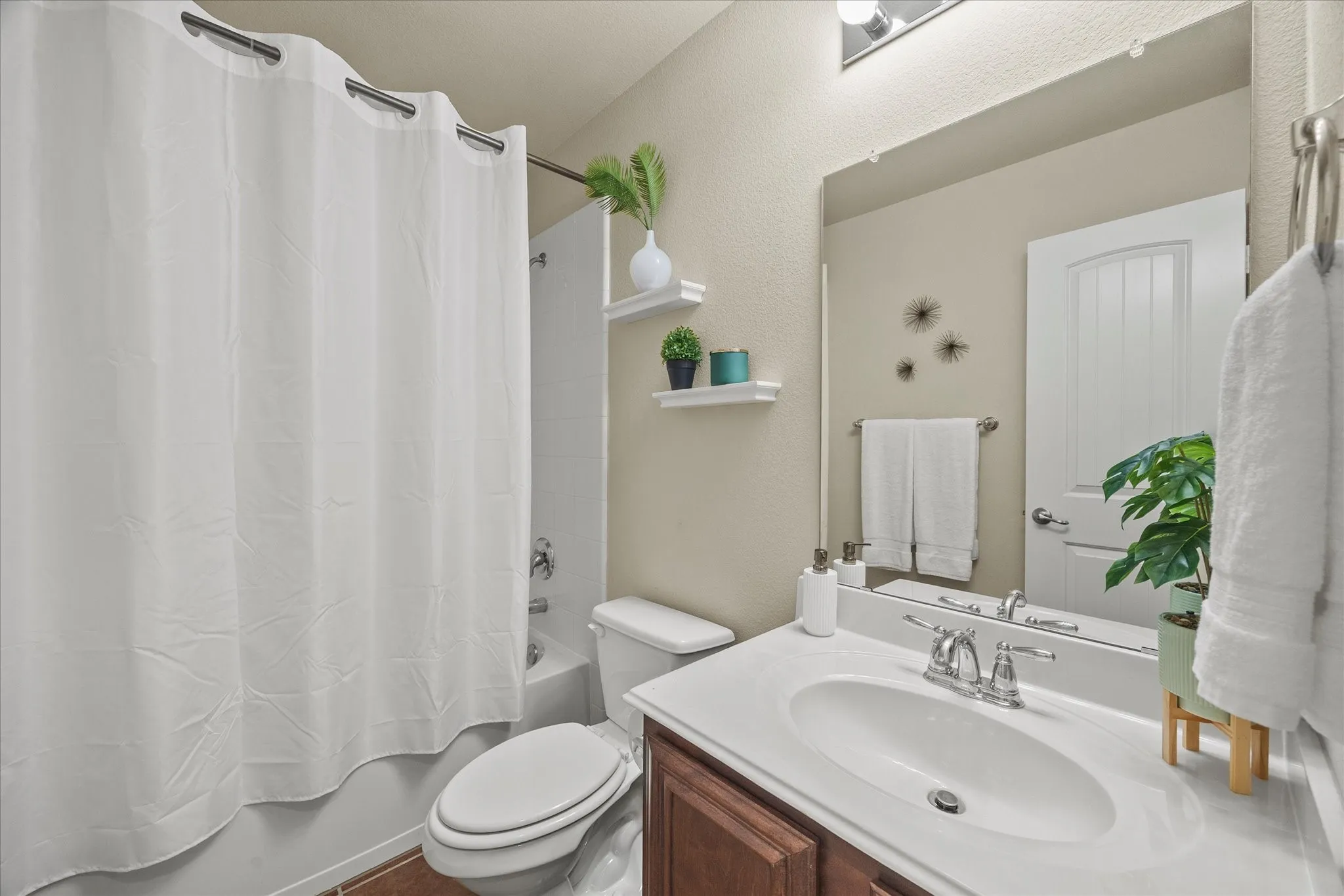 Contemporary bathroom featuring a white porcelain tub/shower combination, built-in shelving, a vanity with a white countertop and integrated sink, and a framed mirror