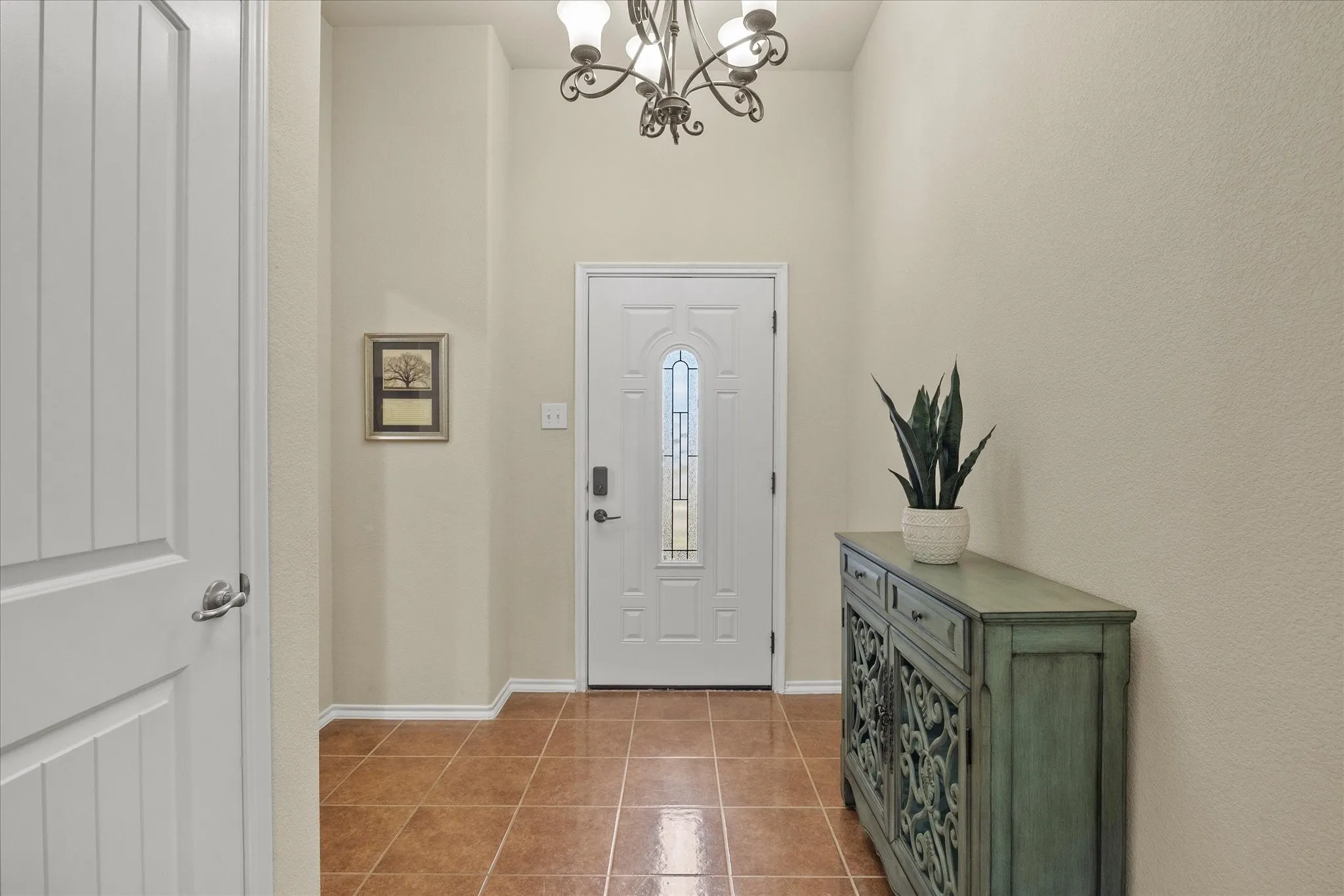 Inviting entryway featuring a white paneled door with decorative glass inserts, terracotta-toned tile flooring, and a wrought iron chandelier