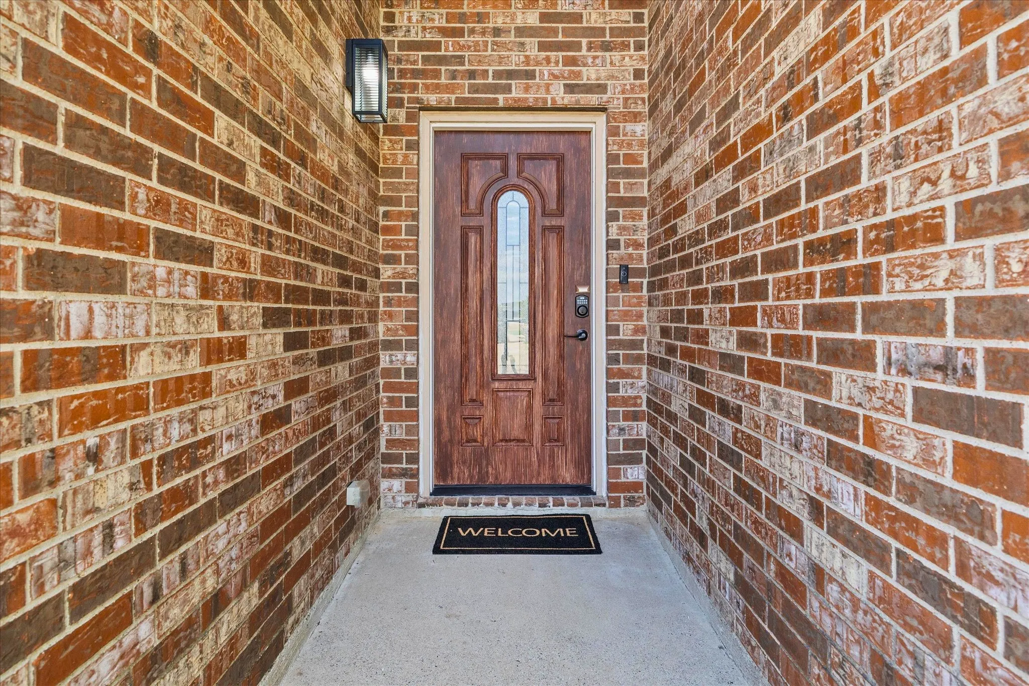 Brick exterior entry with an arch-paneled wood door, frosted glass insert, and a black exterior light fixture