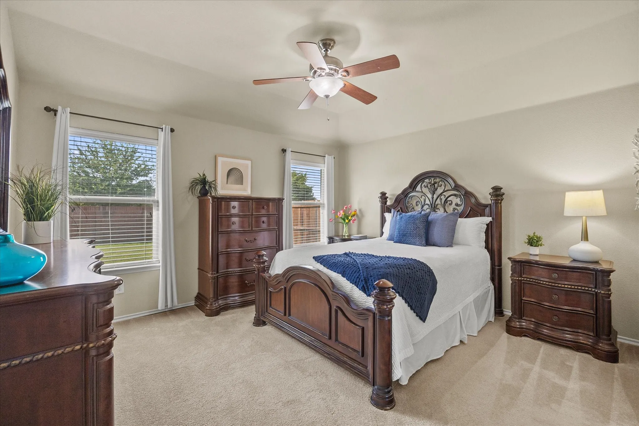 Carpeted bedroom with a ceiling fan, two windows featuring horizontal blinds, and neutral-toned walls