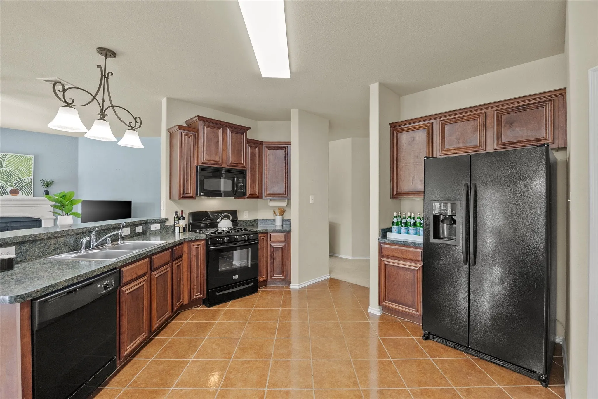 Kitchen featuring rich wood-finish cabinetry, black appliances, a double basin sink, and tile flooring