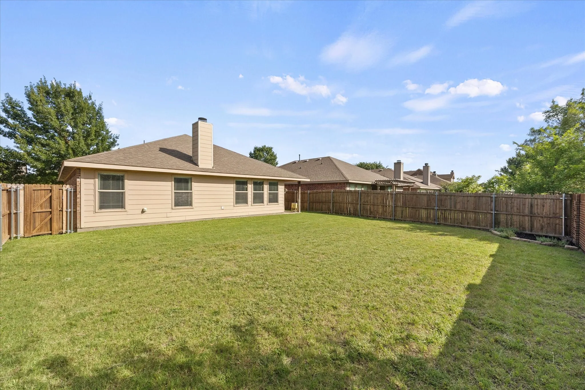 Expansive backyard with a manicured lawn, full wood privacy fencing, and a stucco-finish exterior