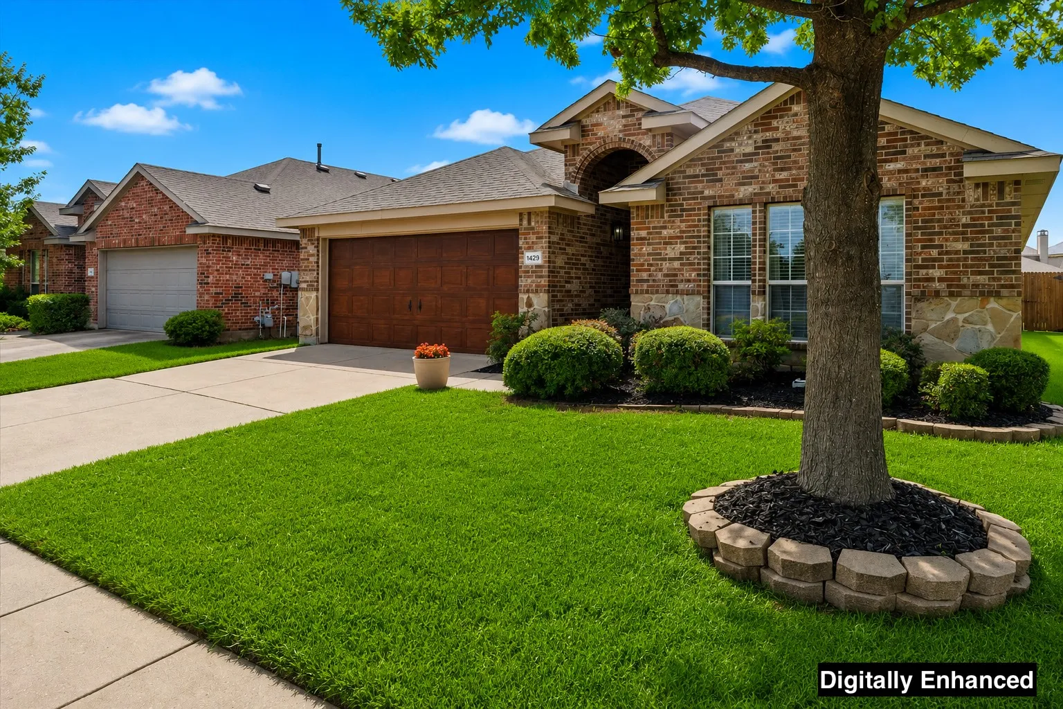 Brick and stone exterior featuring a wood-finish garage door, concrete driveway, and a landscaped front yard with a mature tree