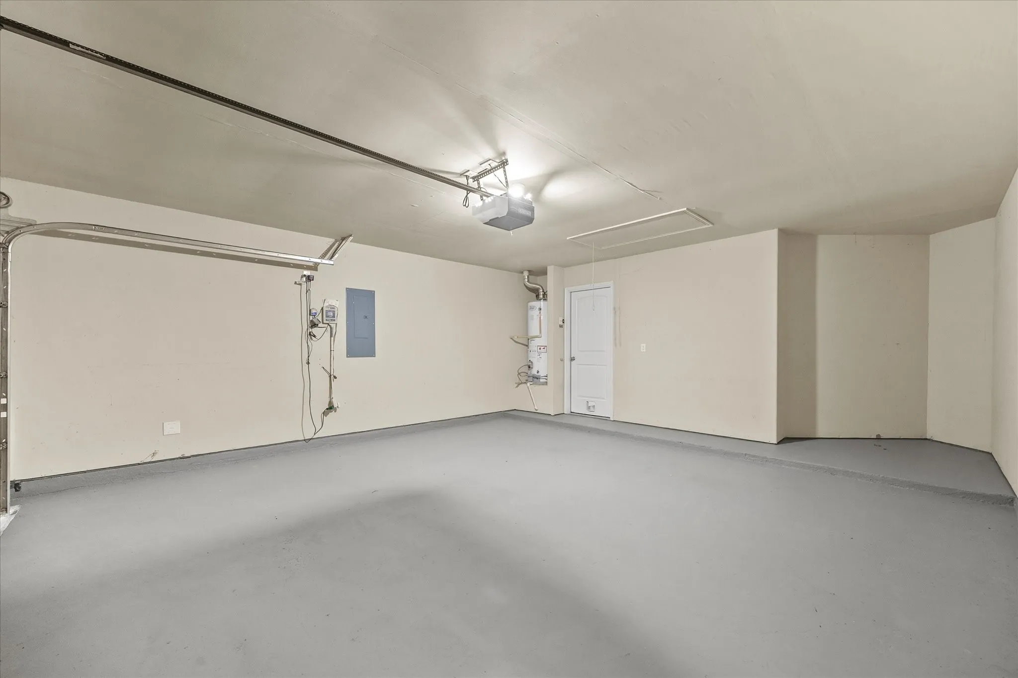 Spacious garage featuring a light gray floor finish, neutral wall paint, overhead garage door mechanism, and a water heater