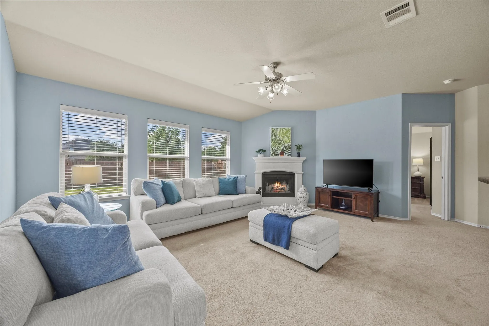 Spacious living area featuring vaulted ceilings, a ceiling fan, carpet flooring, and a white mantel fireplace