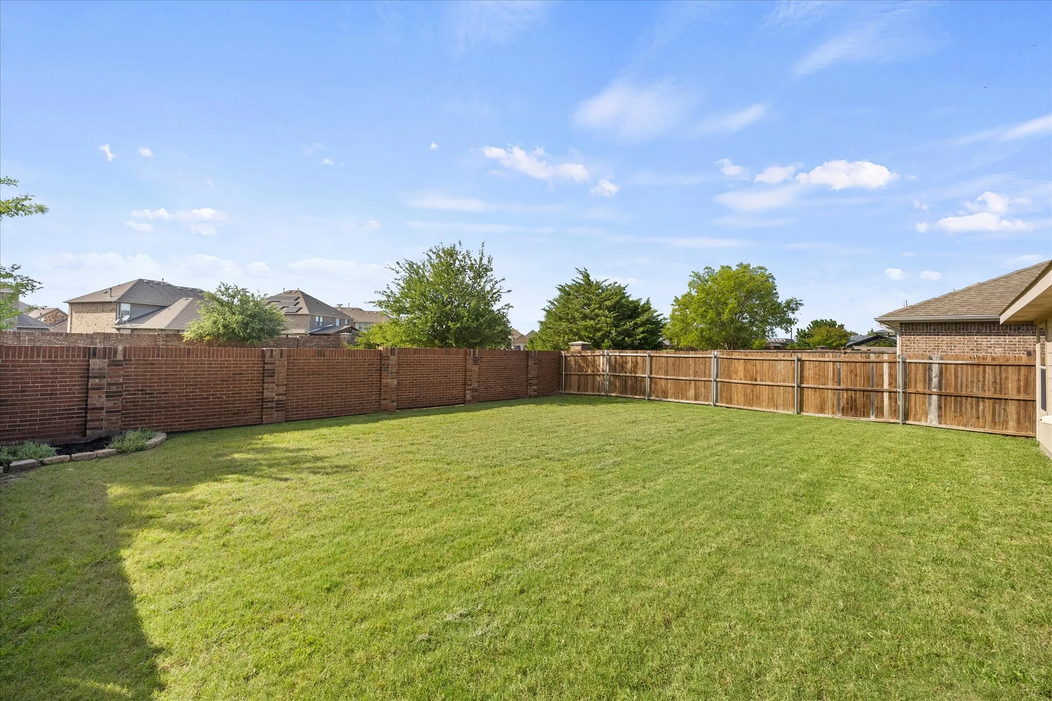Expansive green lawn with a brick perimeter wall, a wood fence, and a landscaped border