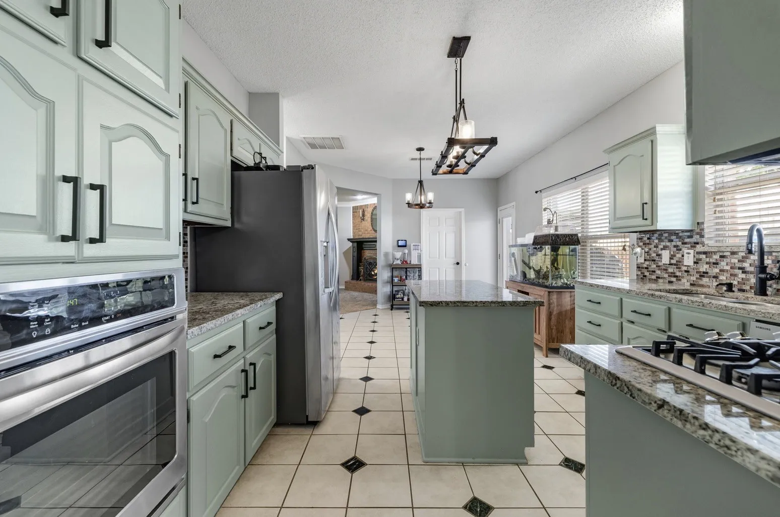 Spacious kitchen featuring light green cabinetry, granite countertops, and stainless steel appliances