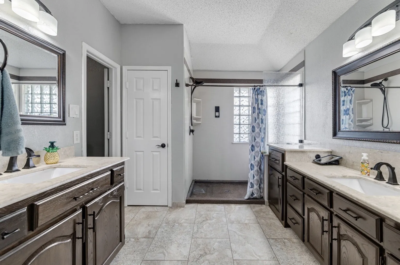 Bathroom featuring dual dark wood vanities with light-toned countertops, undermount sinks, and dark fixtures