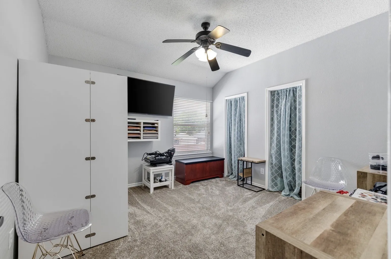 Vaulted ceiling room featuring light gray walls, textured carpet flooring, and a ceiling fan with integrated lighting