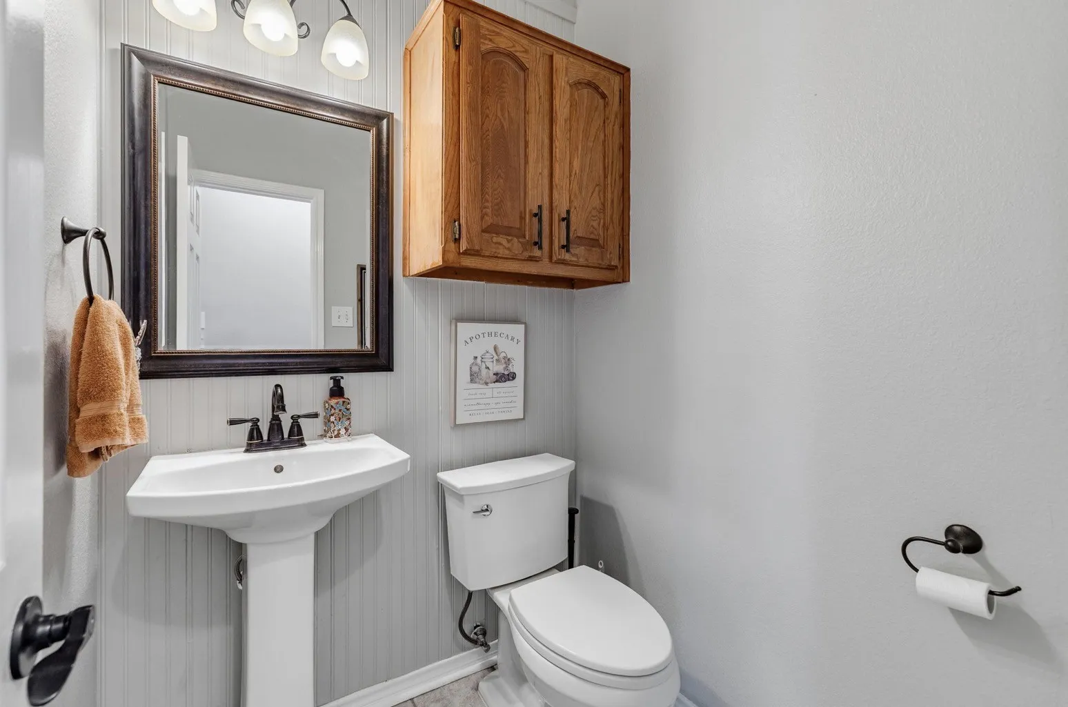 Bathroom featuring a pedestal sink, framed mirror, and wood-finish cabinetry