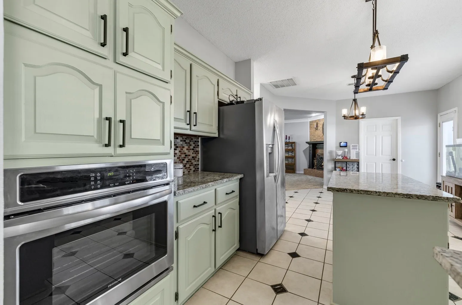 Kitchen with light green cabinetry, stainless steel double wall oven, and a mosaic tile backsplash