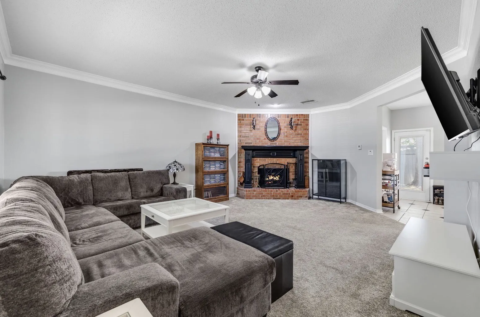 Spacious living area featuring a corner brick fireplace with a black mantel, crown molding, and a ceiling fan with integrated lighting