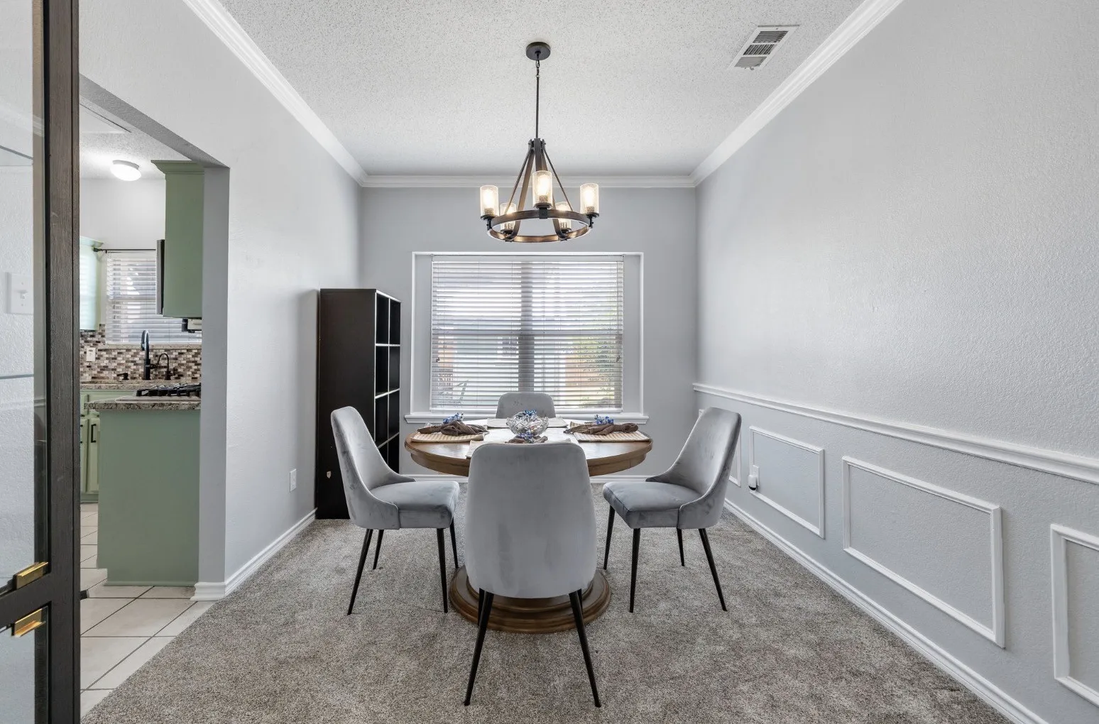 Carpeted dining area featuring wainscoting, crown molding, a modern chandelier, and a window with blinds