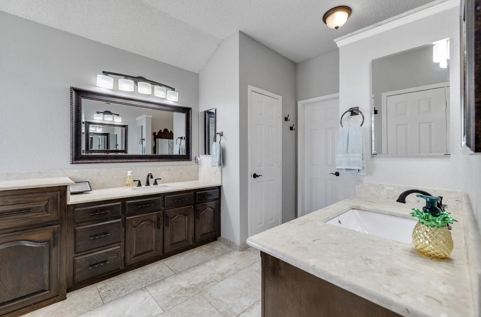 Dual vanity bathroom featuring a light-toned countertop, wood-finish cabinetry, and tiled flooring