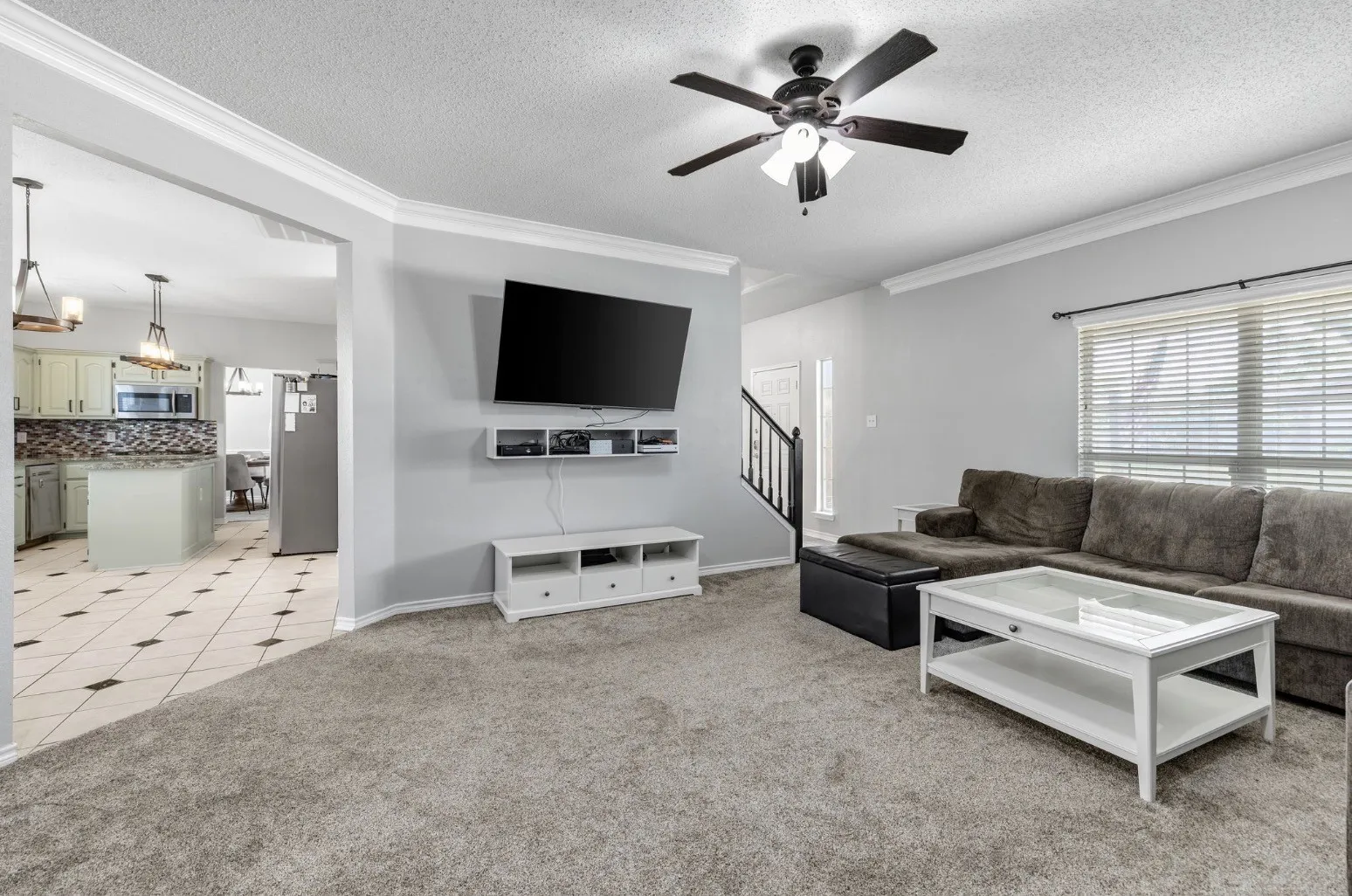 Spacious living area featuring light gray walls, crown molding, and a ceiling fan