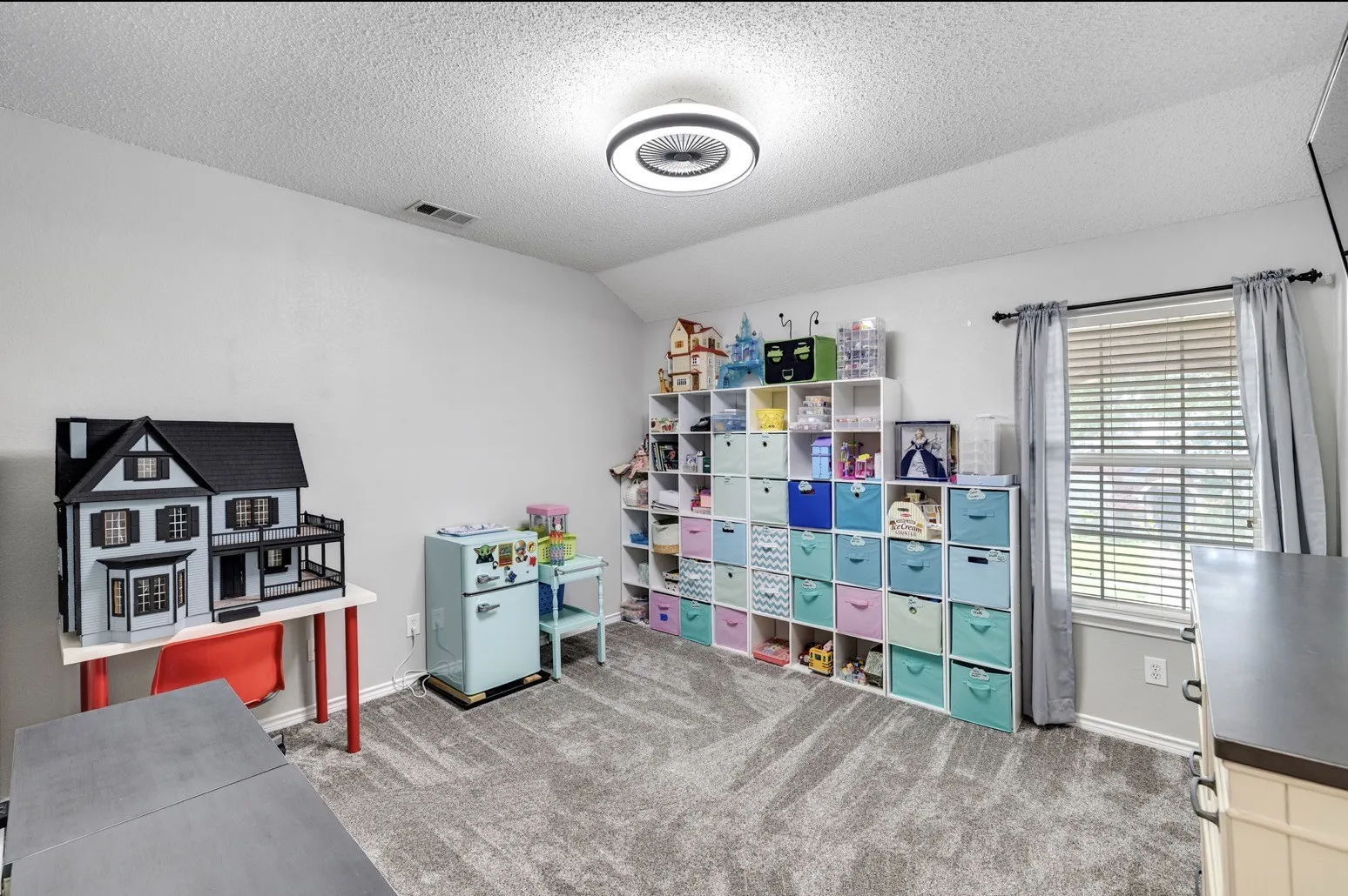 Spacious room featuring light gray wall paint, gray carpeting, a window with blinds and drapes, and a contemporary ceiling light fixture