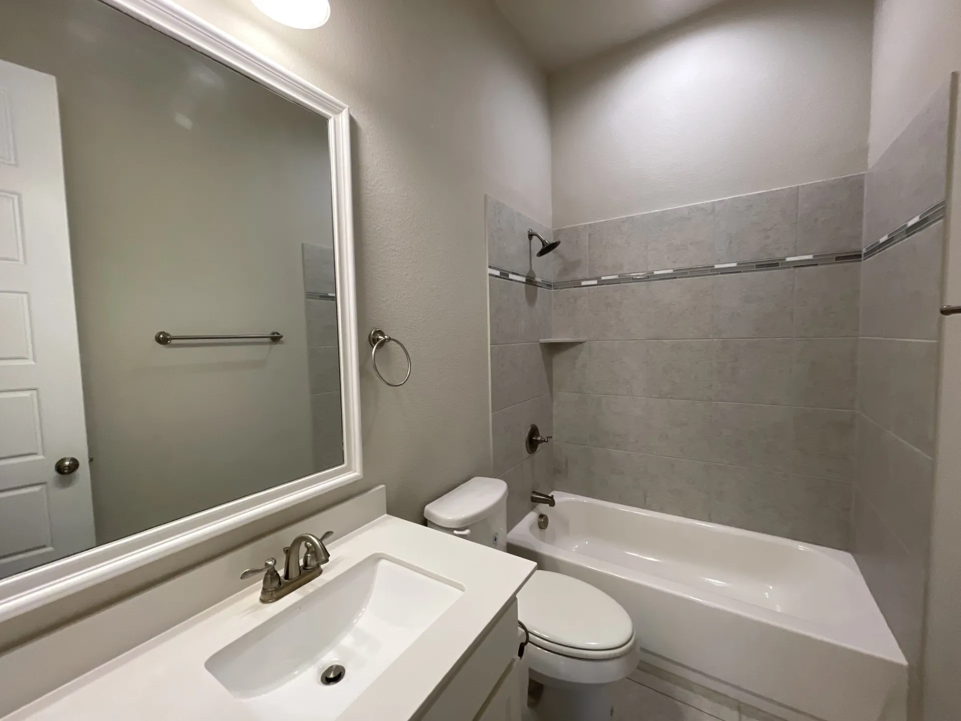 Full bathroom featuring a single vanity with a white countertop and integrated sink, brushed nickel faucet, and a large framed mirror