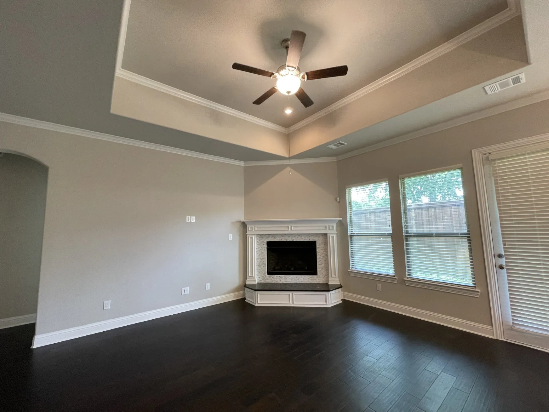 Living area featuring dark wood-finish flooring, a tray ceiling with a ceiling fan, and recessed lighting