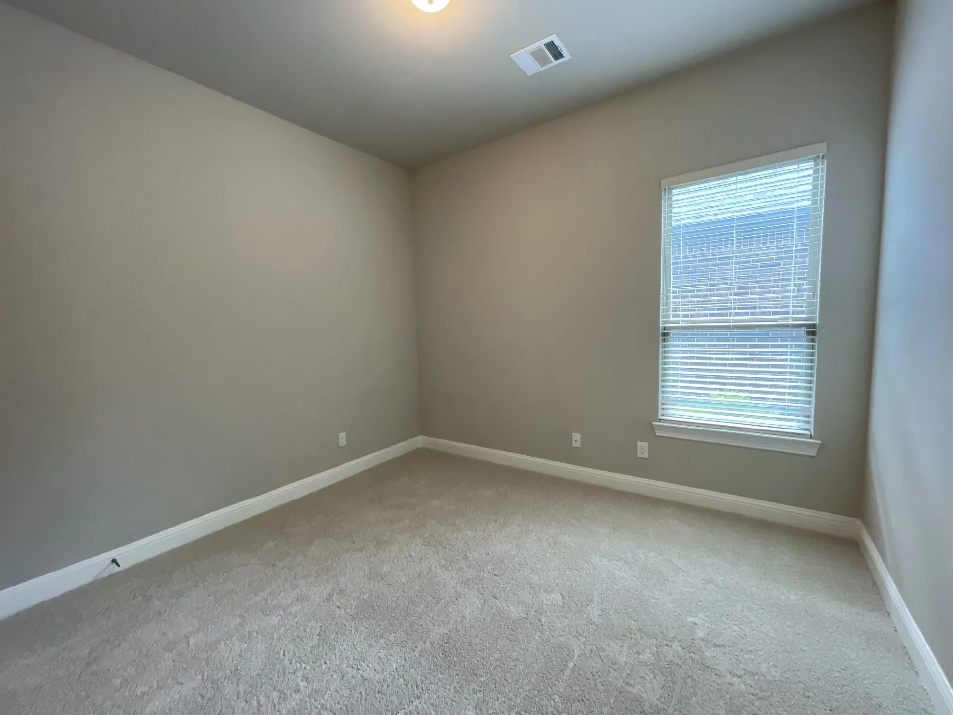 Carpeted interior room featuring neutral wall paint, white baseboards, and a single window with horizontal blinds