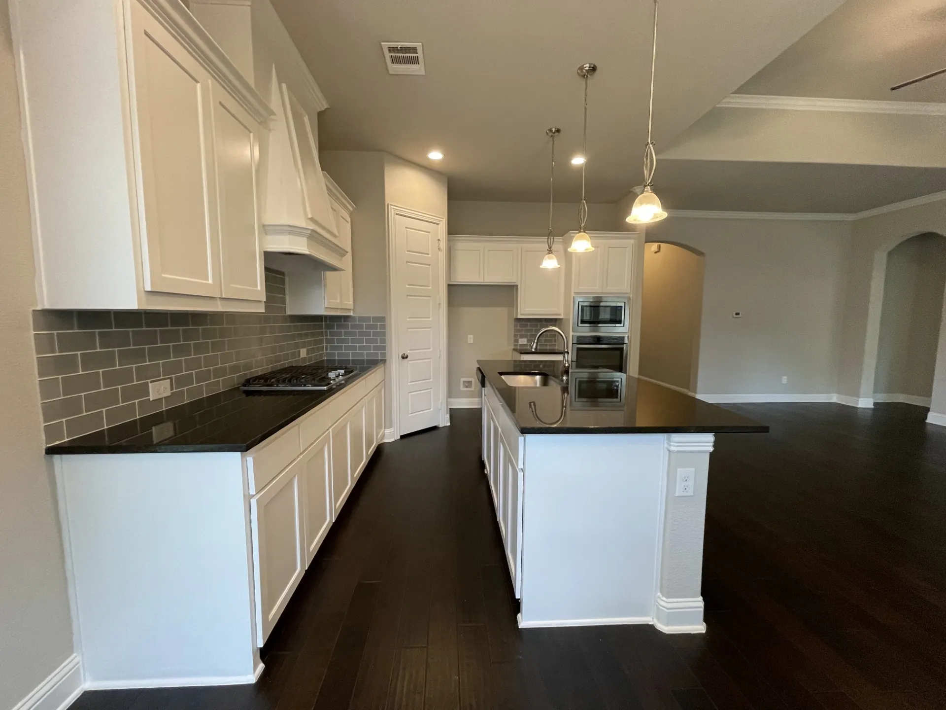 Kitchen featuring dark wood-finish flooring, white cabinetry, dark countertops, and a subway tile backsplash