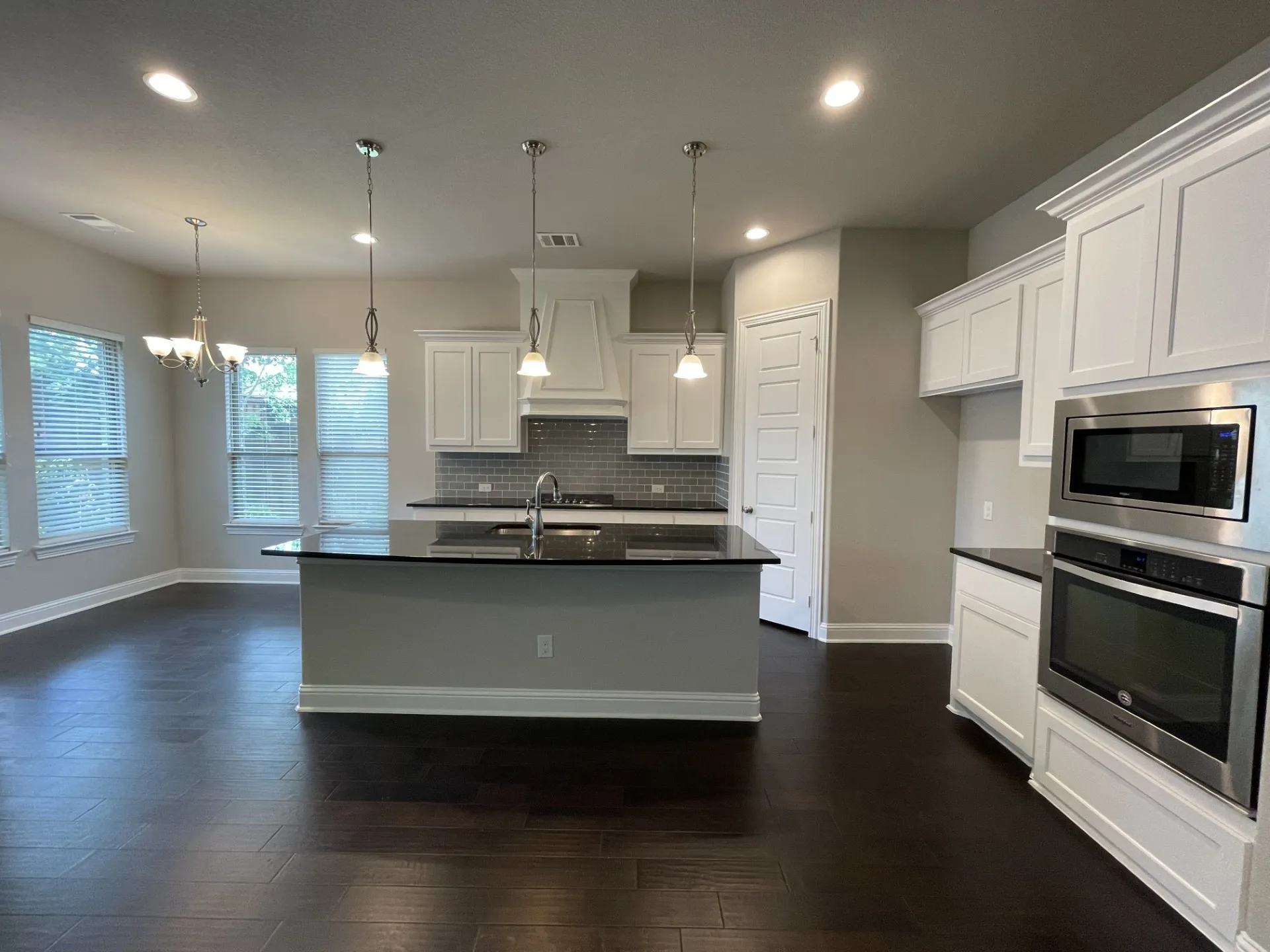 Spacious kitchen featuring an island with a sink and pendant lighting, stainless steel appliances, white cabinetry, and dark wood-finish flooring
