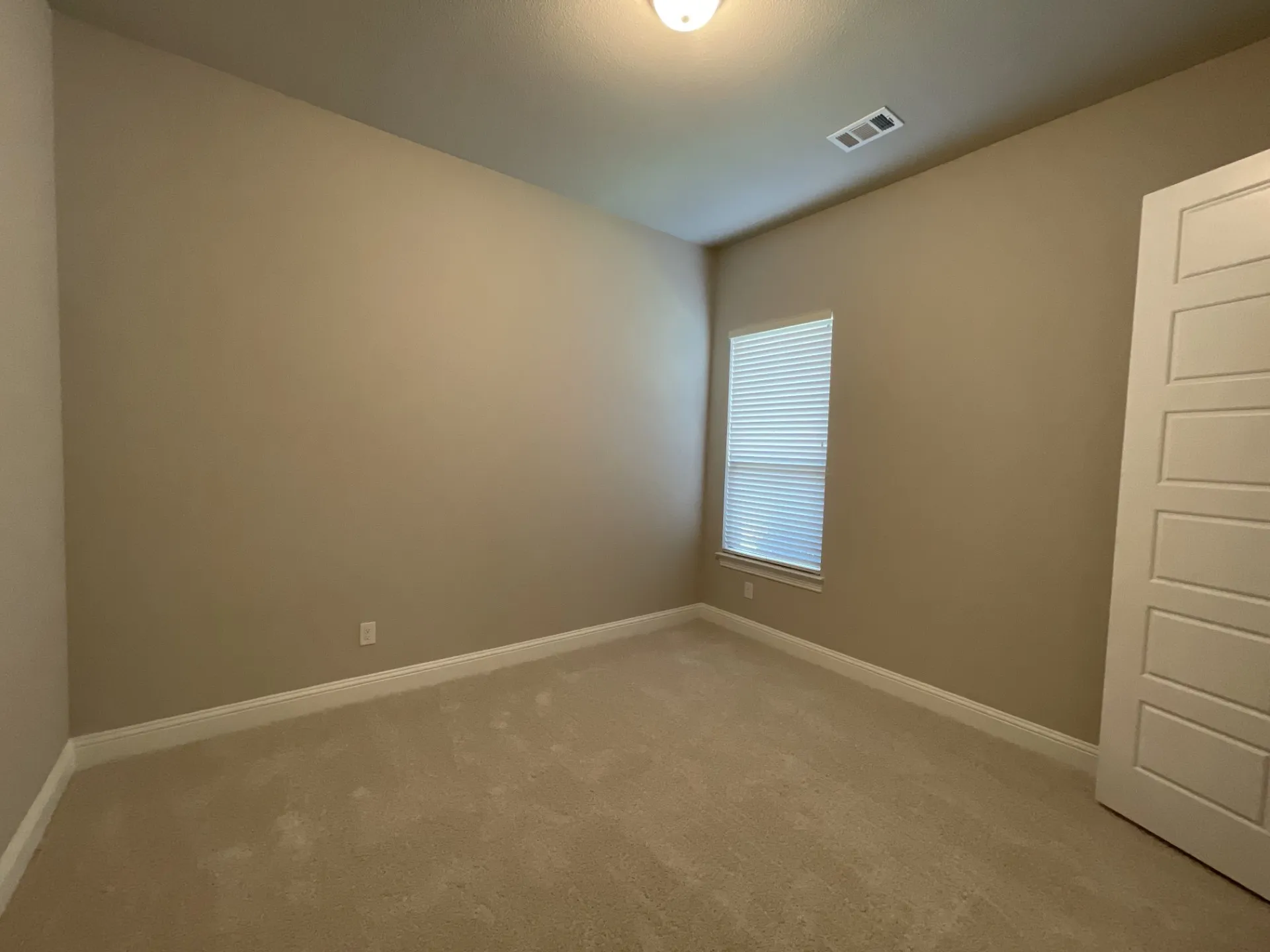 Carpeted interior room featuring neutral wall tones and a single window with horizontal blinds