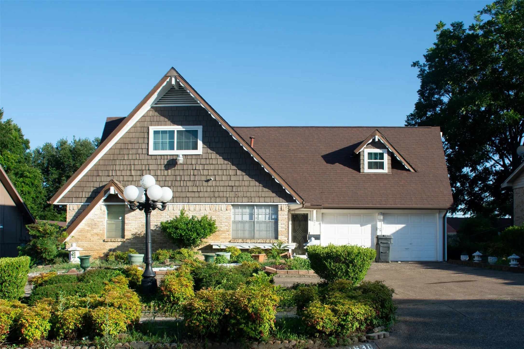 Two-story residence featuring a shingle roof, brick and shingle siding, a two-car garage, and a dormer window