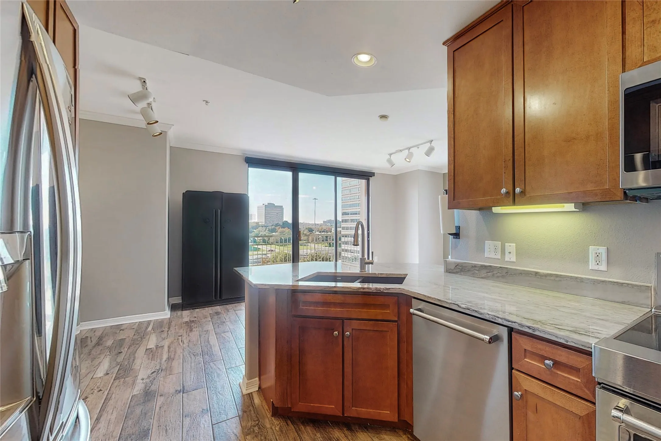 Kitchen featuring sink, light stone counters, appliances with stainless steel finishes, kitchen peninsula, and light hardwood / wood-style floors