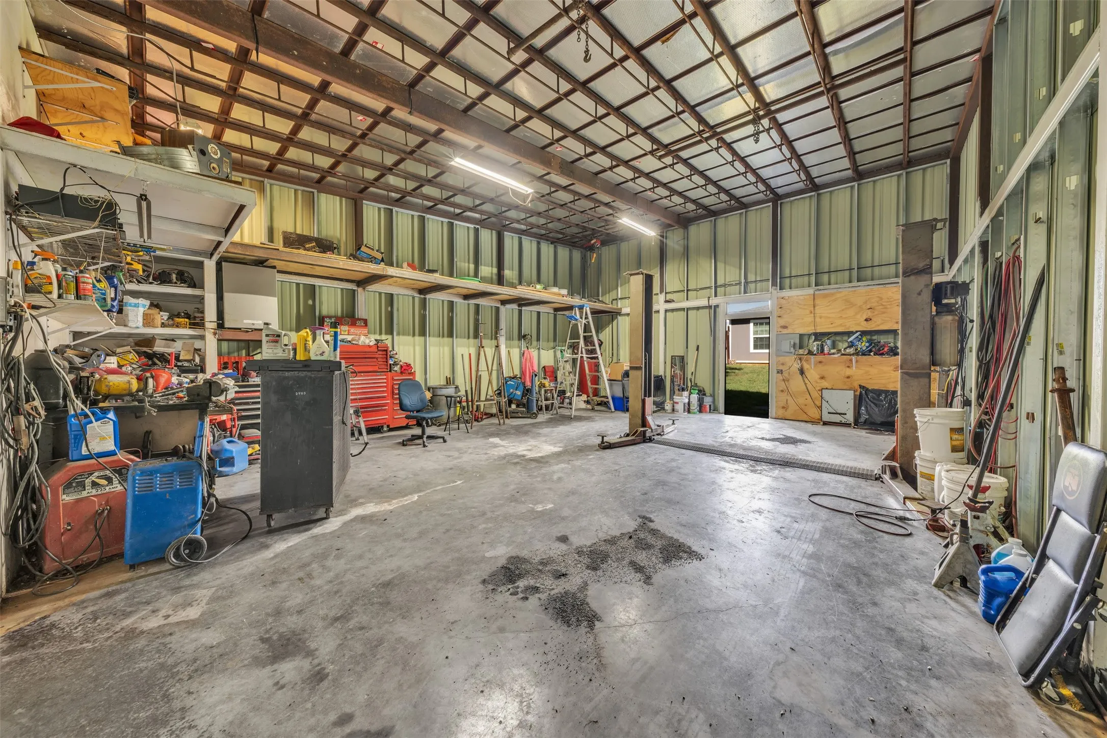 Expansive industrial-style interior featuring a concrete floor, a metal-paneled ceiling with exposed beams, and fluorescent lighting