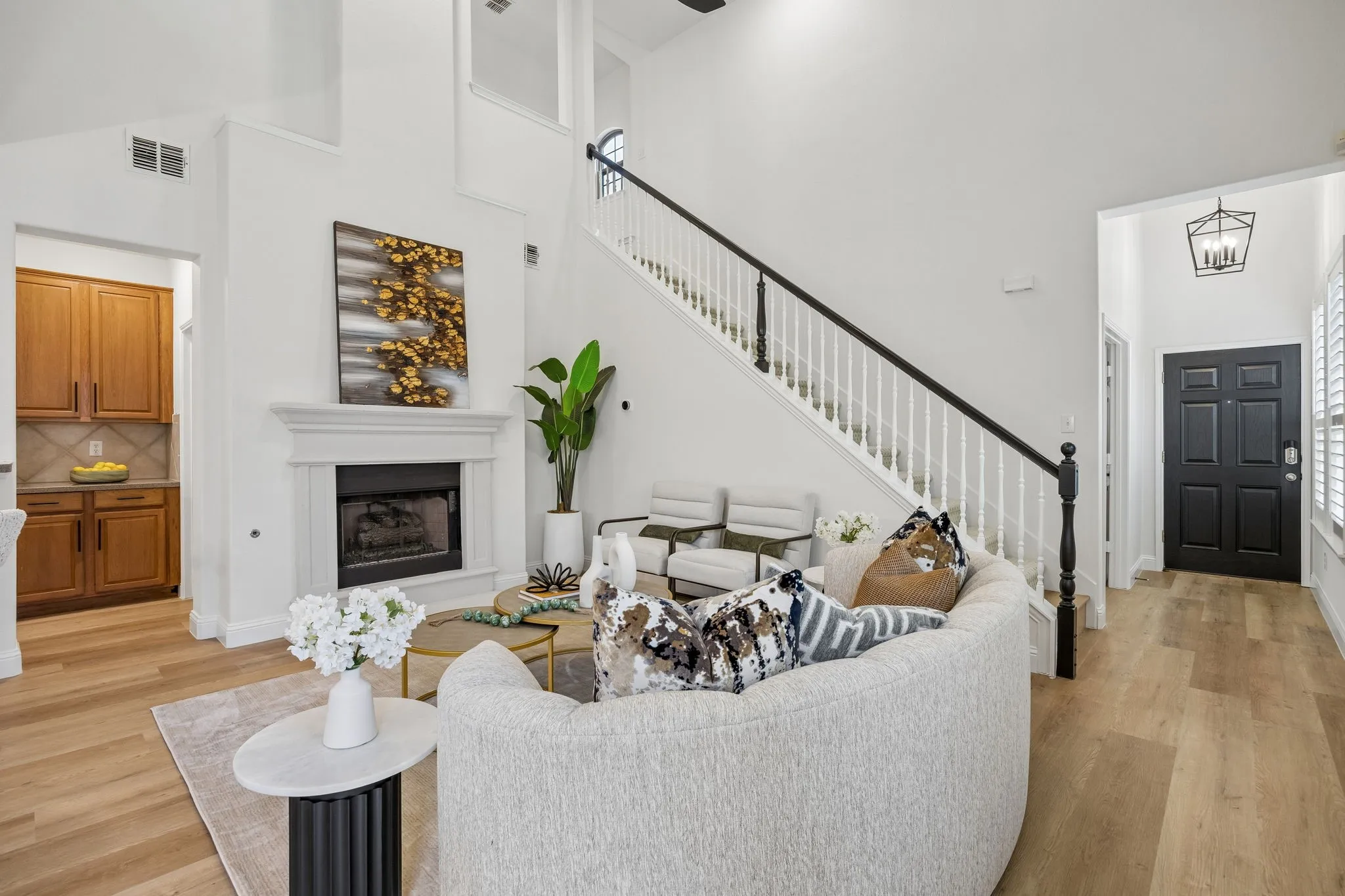 Vaulted ceiling living area featuring a fireplace with a white mantel, wood-finish flooring, and a staircase with white spindles and a black handrail