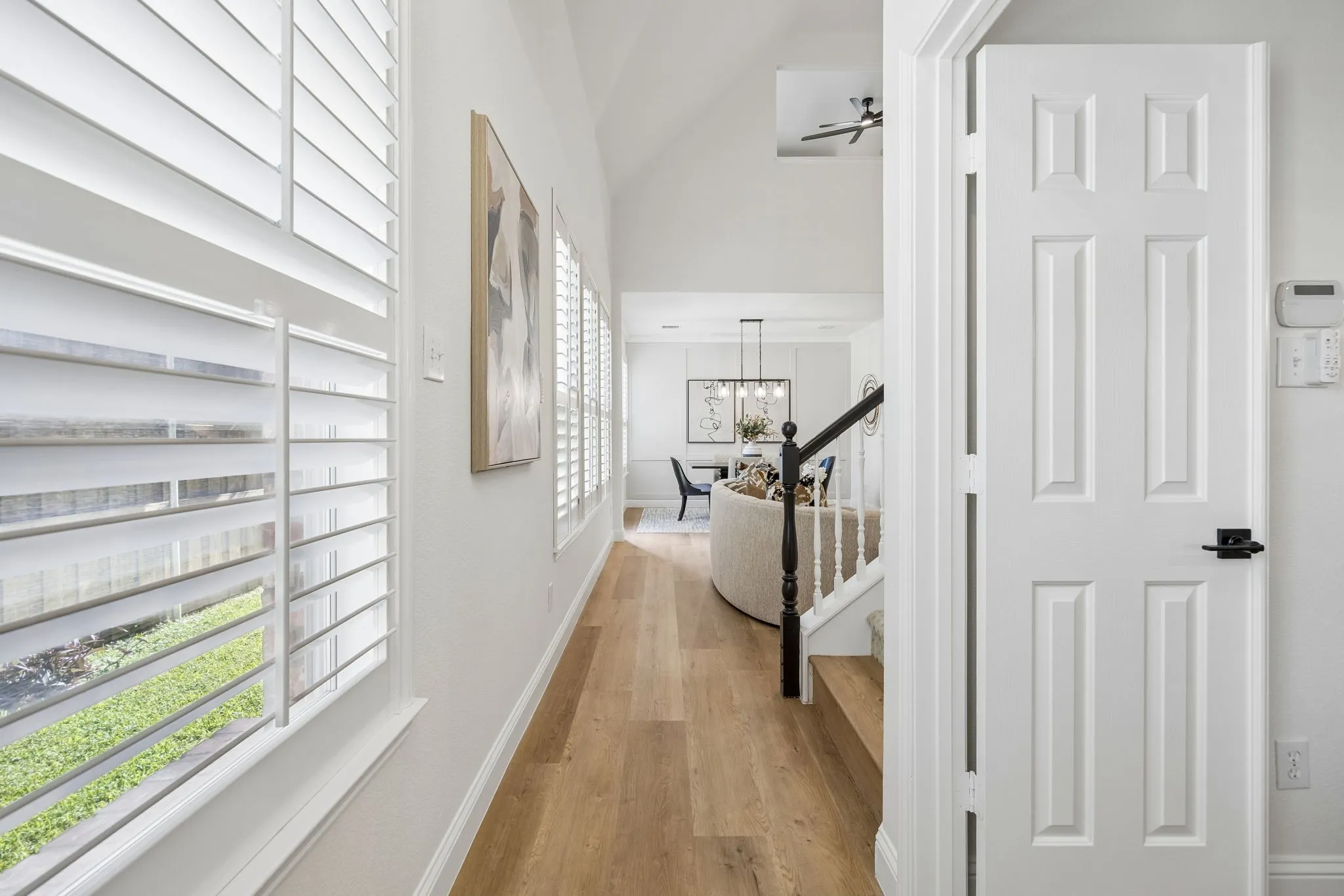 Hallway featuring wood-finish flooring, white plantation shutters, a vaulted ceiling, and a traditional banister with black newel post