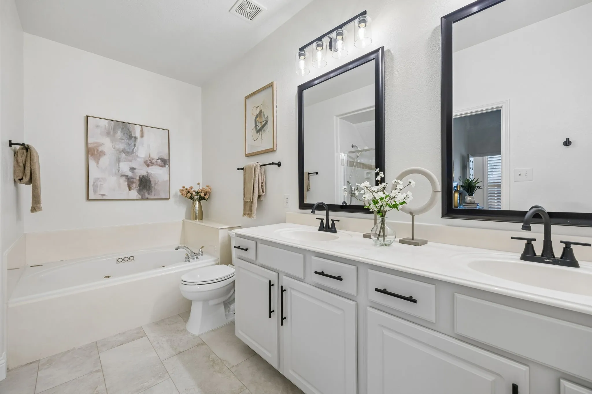 Bathroom featuring a dual vanity with white cabinetry, black hardware, and an integrated countertop