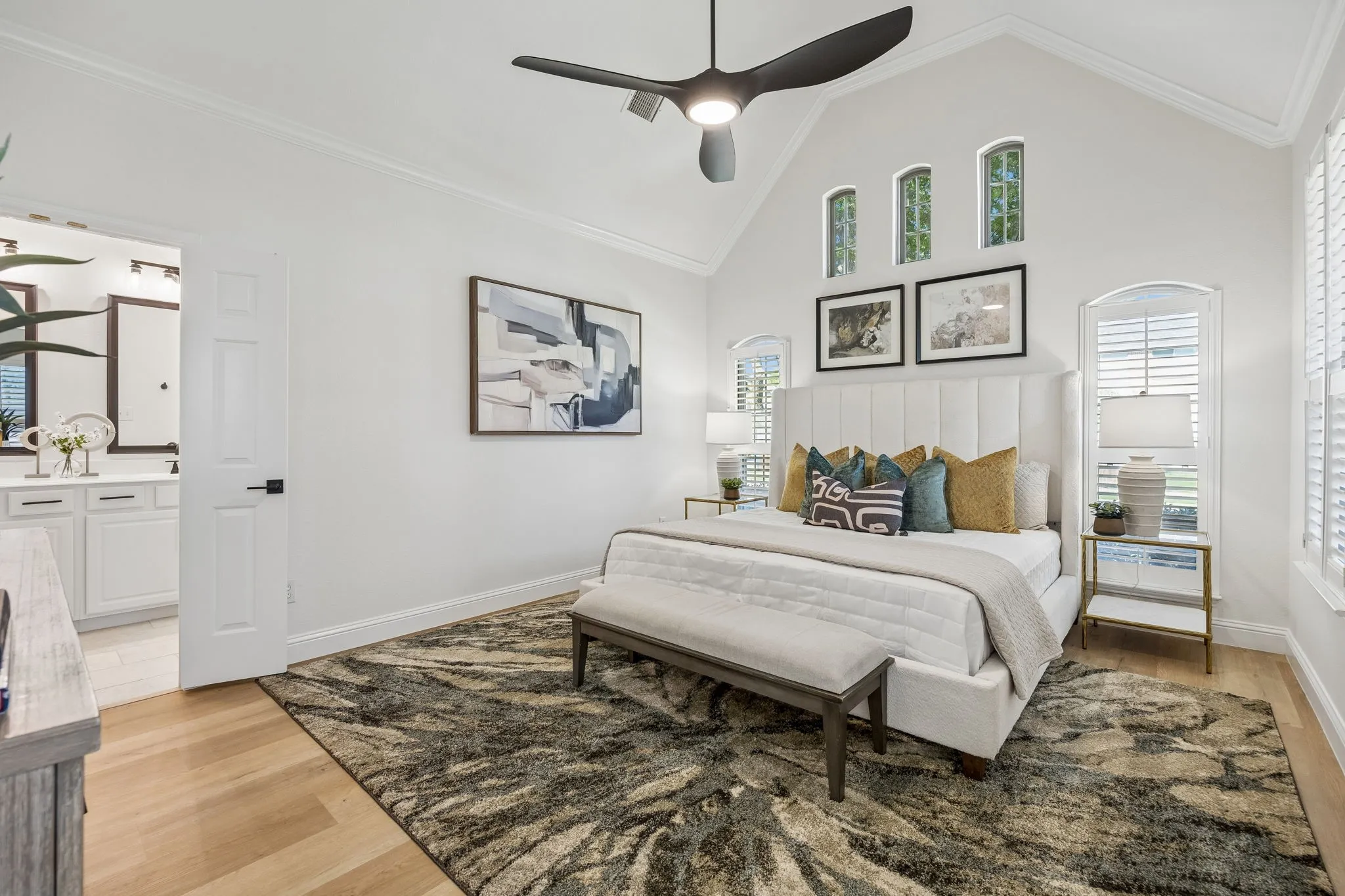 Vaulted ceiling bedroom featuring wood-finish flooring, a contemporary ceiling fan, and arched windows with plantation shutters