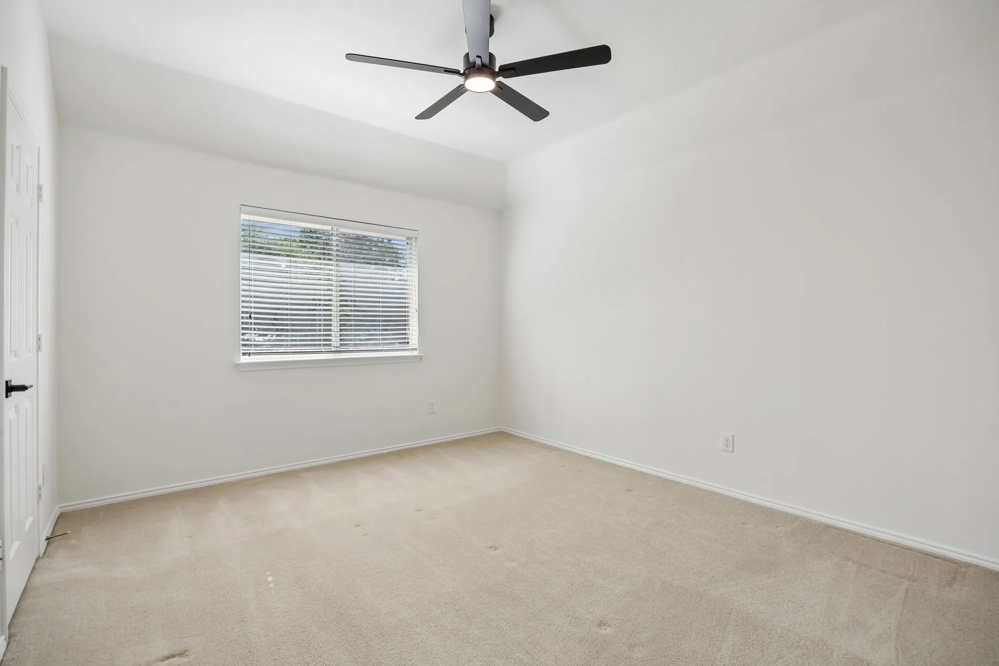 Bright room featuring light-toned carpeting, white walls, and a window with horizontal blinds