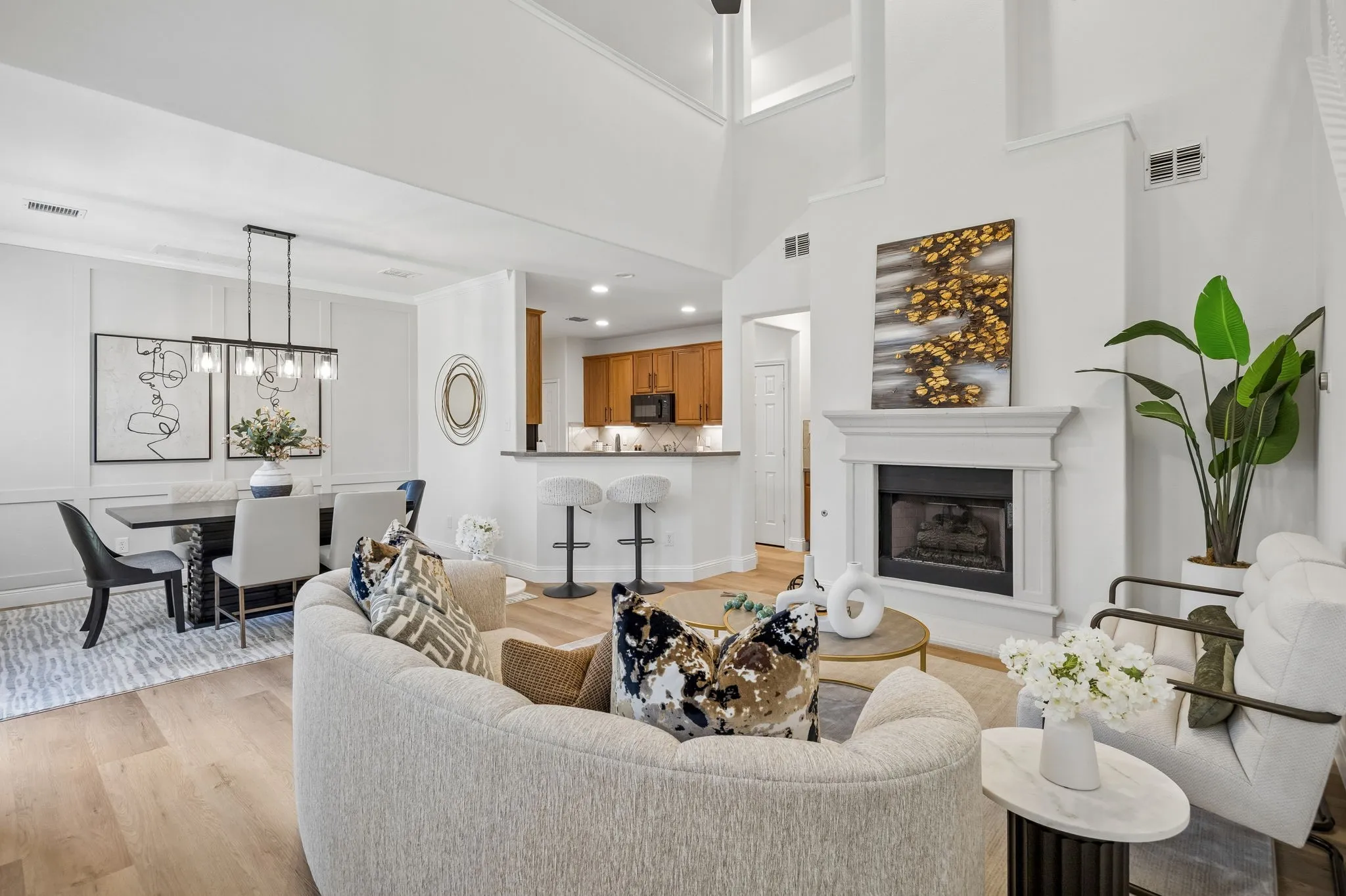 Open-concept living space featuring wood-finish flooring, a two-story ceiling, a fireplace with a white mantel, an integrated kitchen bar, and a dining area with wainscoting