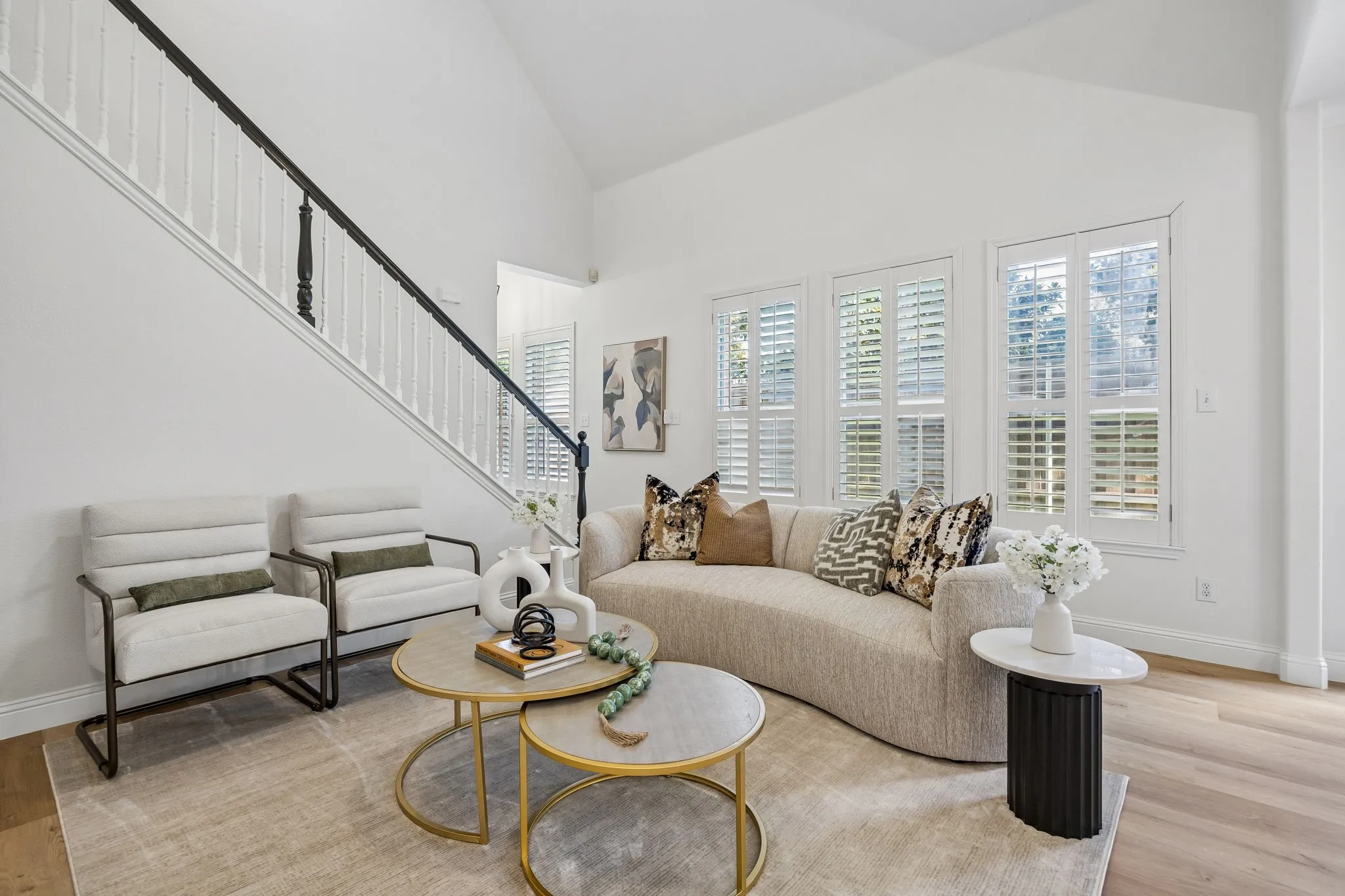 Vaulted ceiling living space featuring wood-finish flooring, white walls, and a staircase with white spindles and a dark handrail