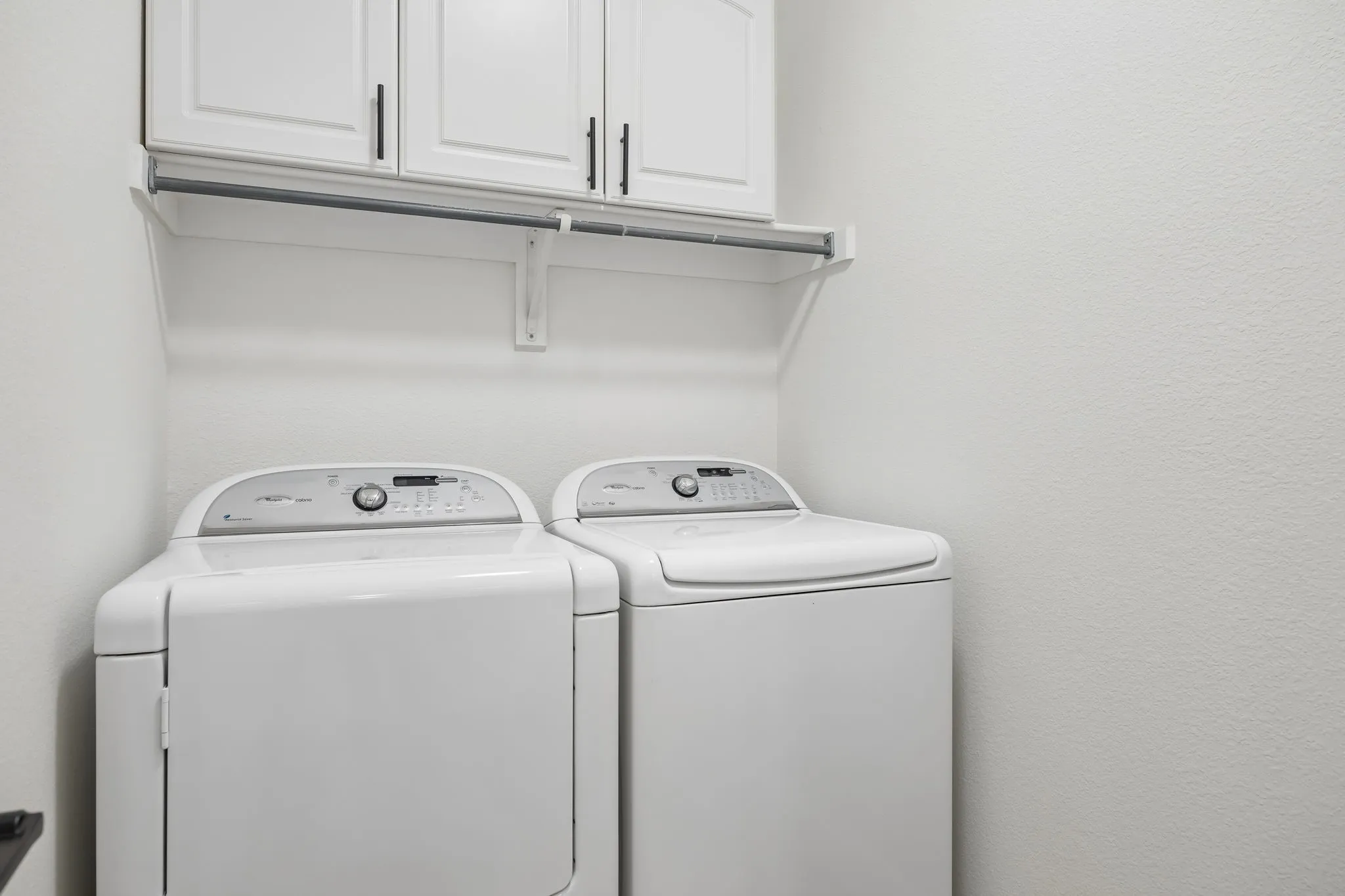 Dedicated laundry area featuring white cabinetry with black hardware, a clothing rod, and neutral wall finishes
